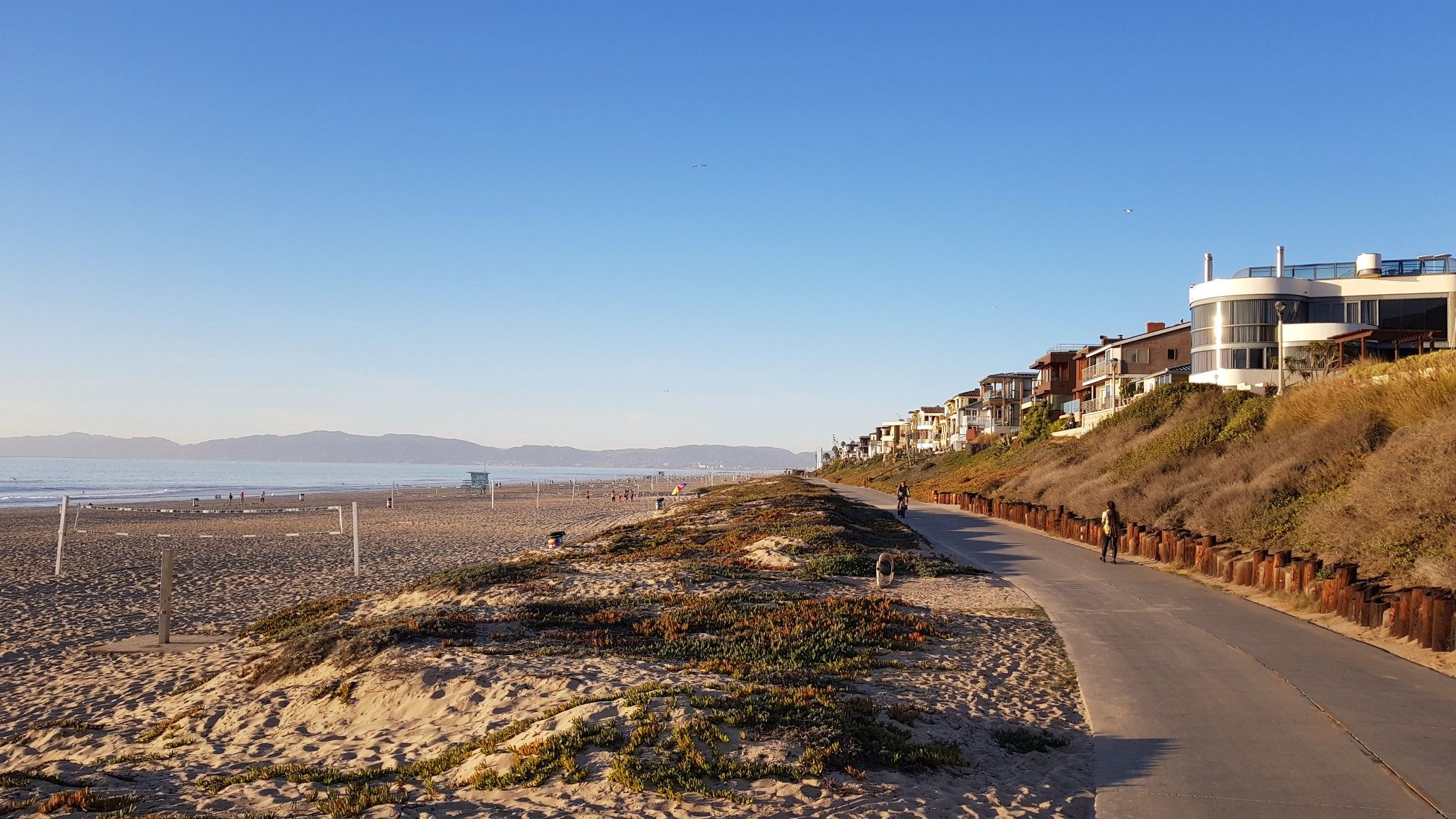 A paved beach path next to sand dunes, houses, and distant mountains on a sunny day. - Palos Verdes Classic Donut Loop