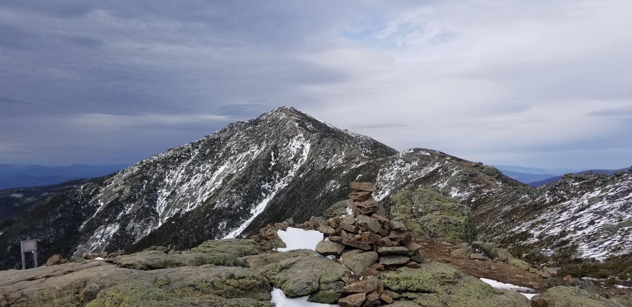 Snowy mountain peak with a rock cairn under a cloudy sky. - Franconia Ridge Loop