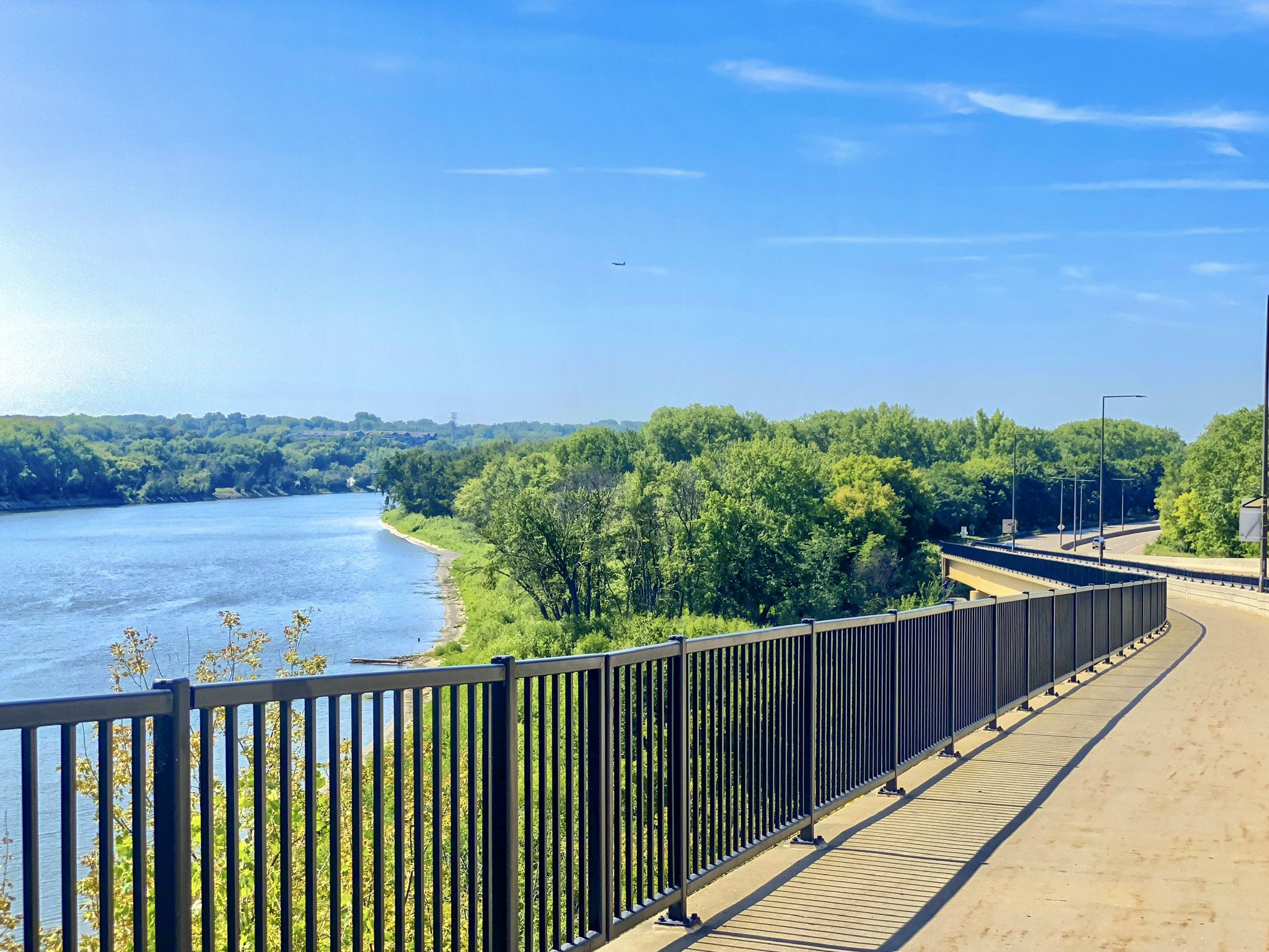 Sunny paved path with a black fence overlooking a river and green forests. - Mississippi River Overlook – Fort Snelling Scenic Overlook loop from Victoria Street