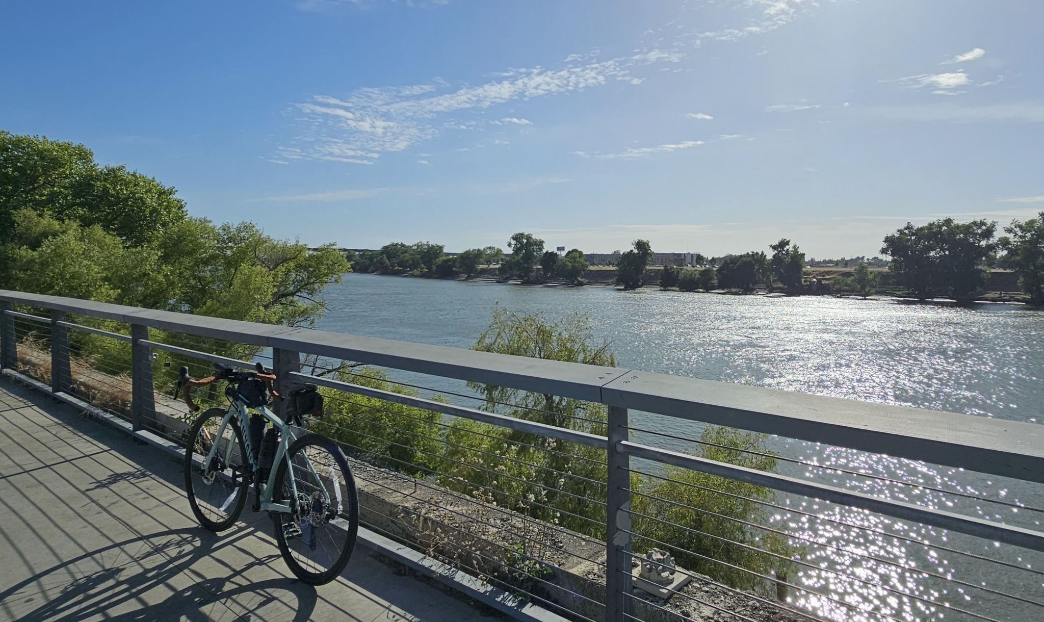 A bicycle rests on a bridge railing overlooking a wide, sunny river. - Sacramento River and Land Park Loop