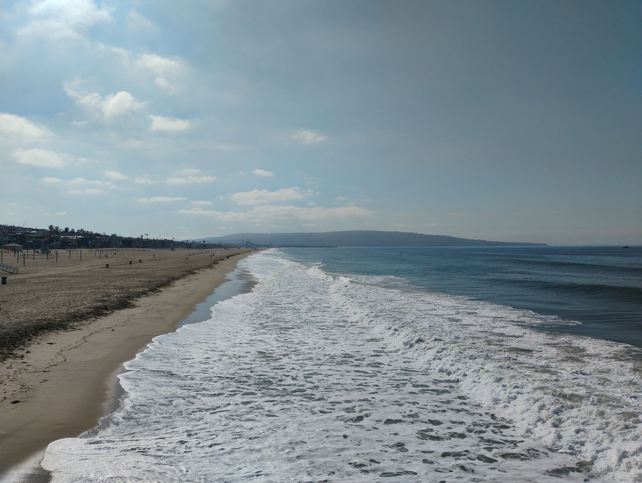 Ocean waves crash on a wide sandy beach under a partly cloudy sky. - Manhattan Beach and Pier loop from Douglas