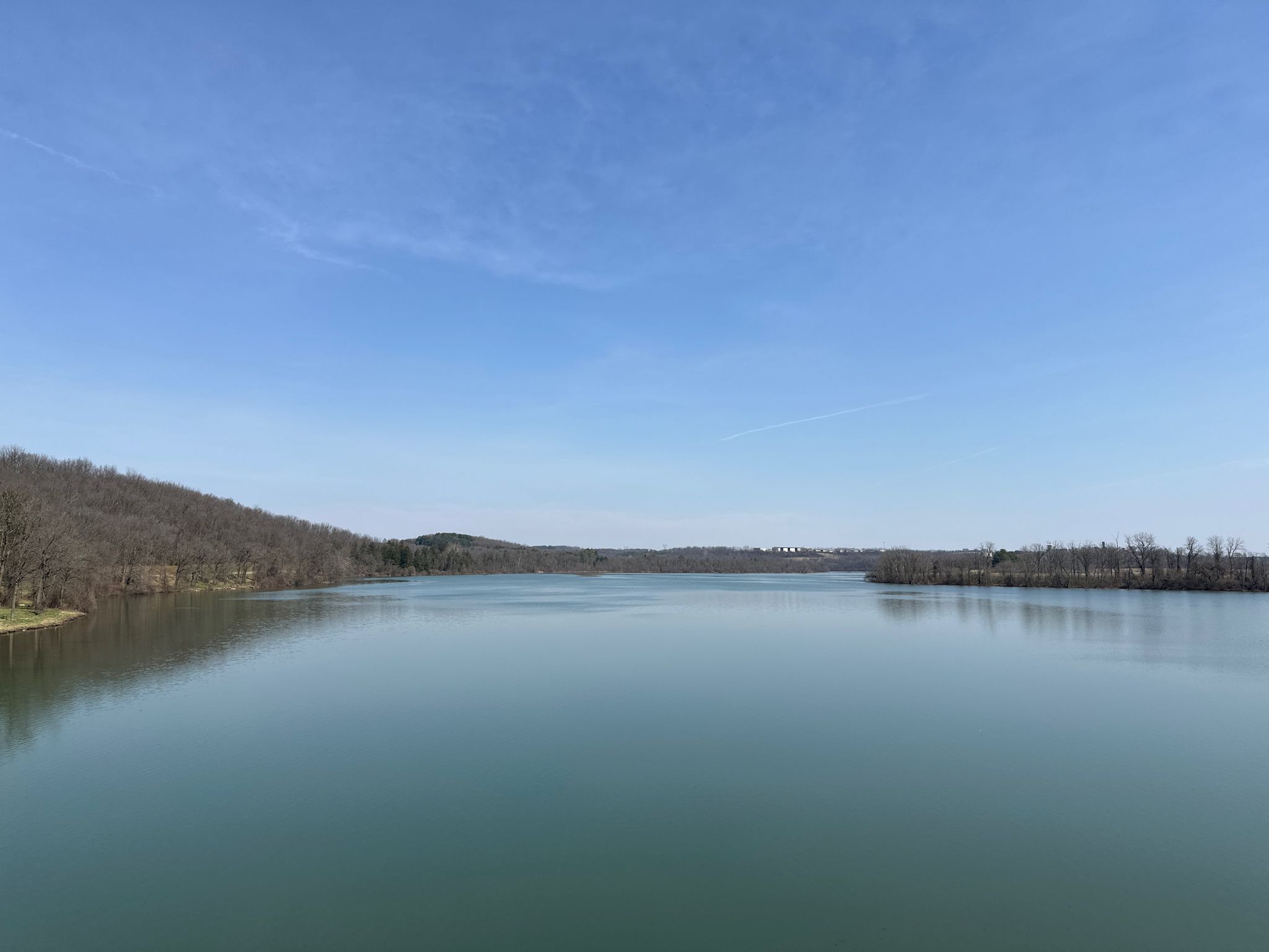 Wide view of a calm lake surrounded by wooded hills under a clear blue sky. - Maiden Creek loop