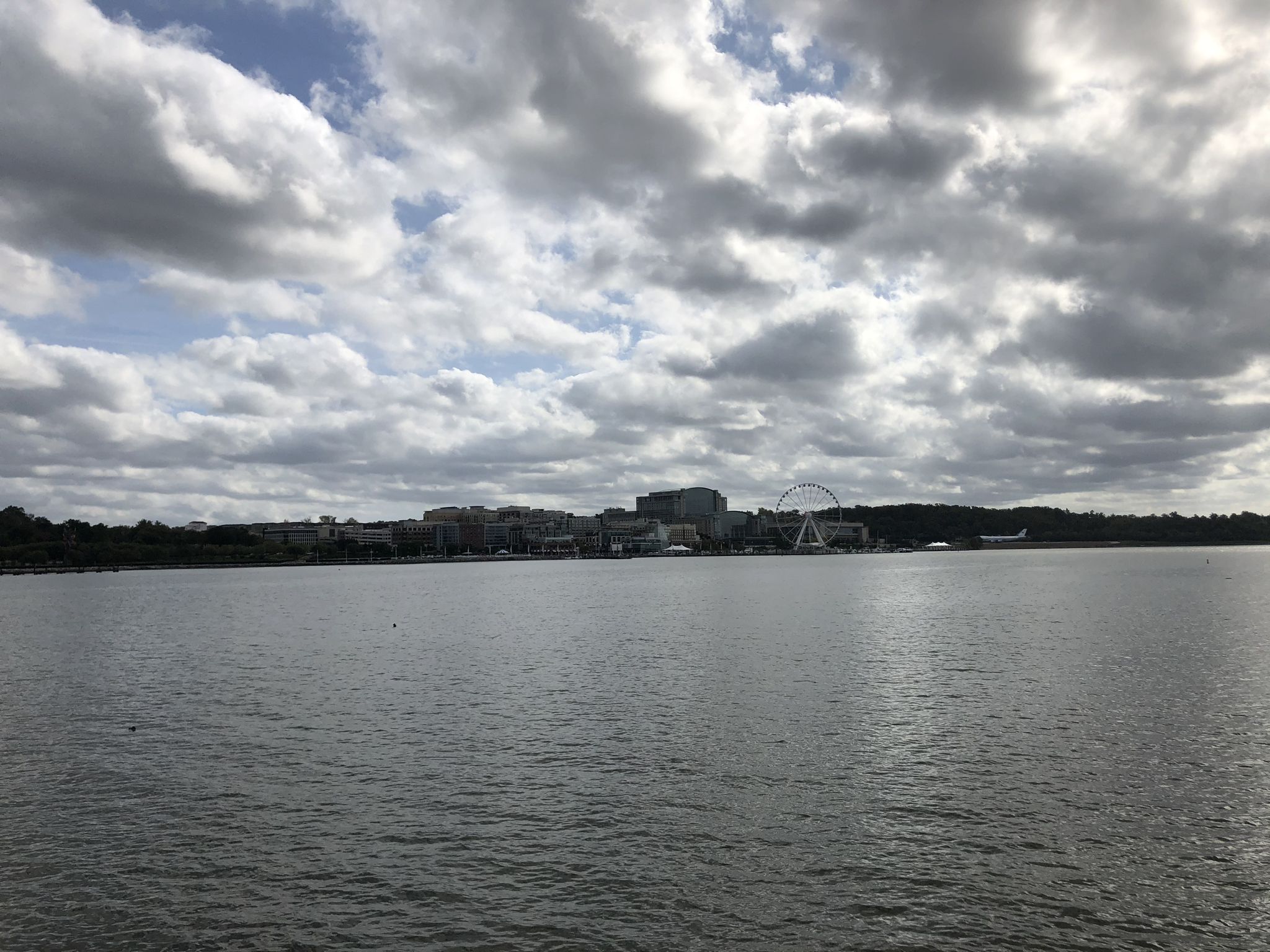 Wide river with a distant city skyline and Ferris wheel under cloudy sky. - View to National Harbor – Corkscrew loop from National Harbor