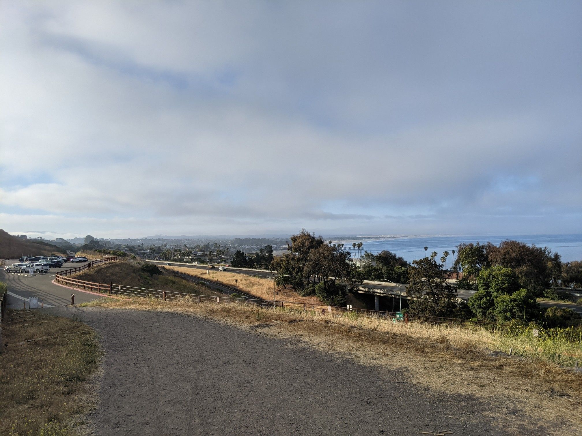 Dirt path overlooking a coastal town and ocean under a cloudy sky. - Adam Hill Memorial Bench – Lone Oak loop from Pismo Beach