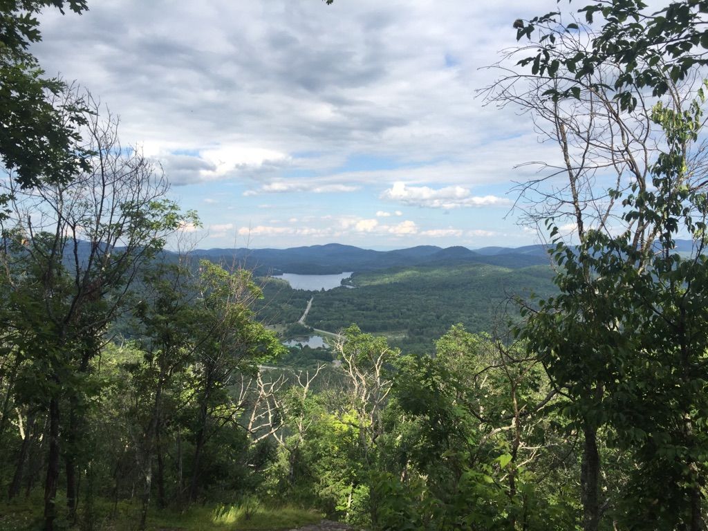 Panoramic view of a lake nestled among green forested mountains under a cloudy sky. - Severance Mountain