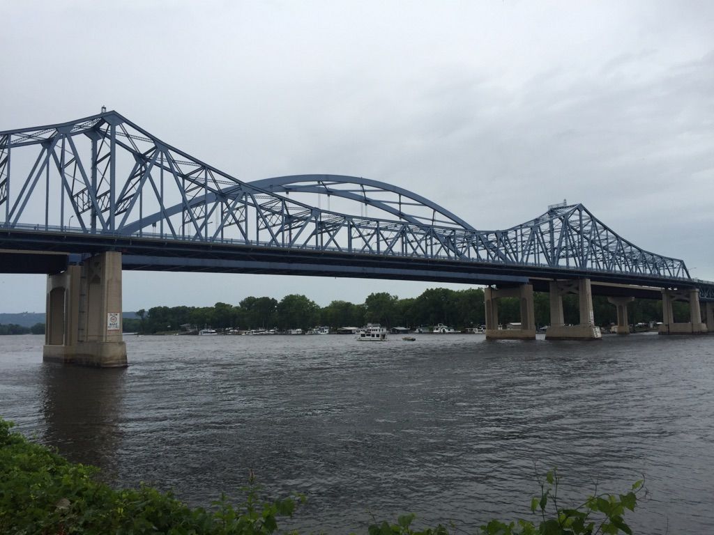 Large blue truss bridge over a wide river with boats, under overcast sky. - Running loop from La Crosse