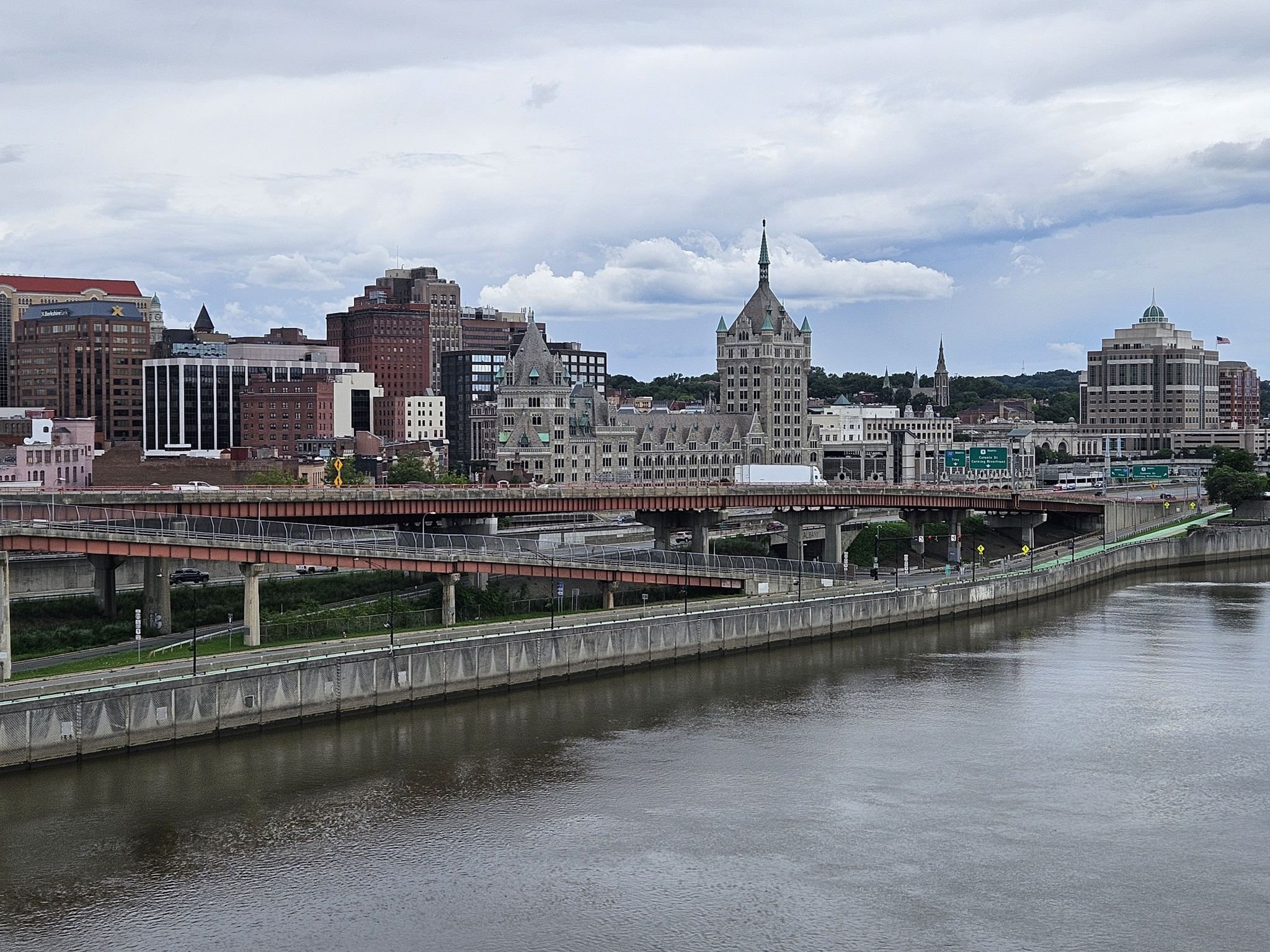 City skyline with tall buildings, bridges, and a wide river under cloudy skies. - Albany-Hudson Electric Trail and Nassau Lake Loop