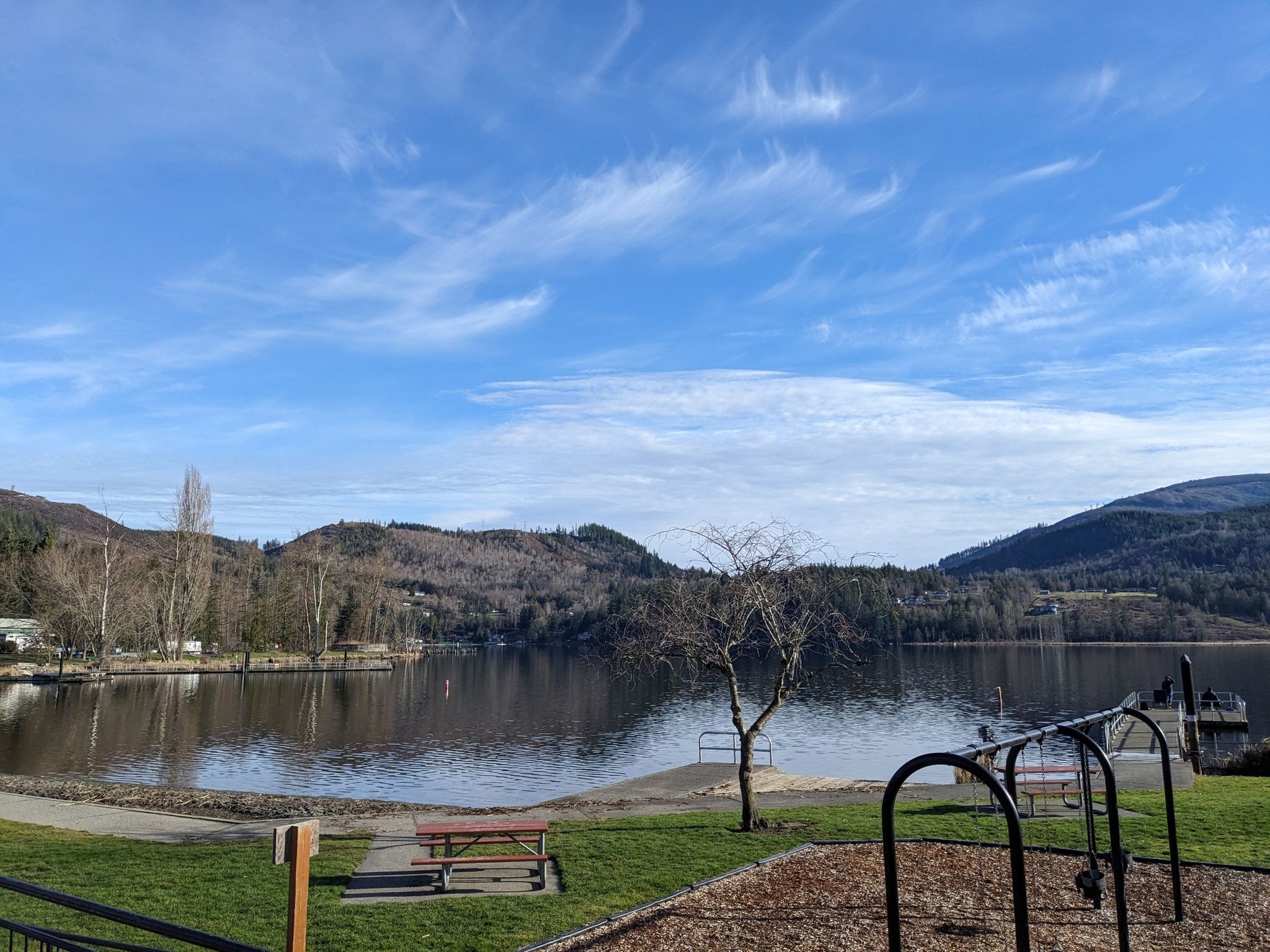 Sunny lake with distant mountains, a picnic table, and playground equipment. - Skagit Valley
