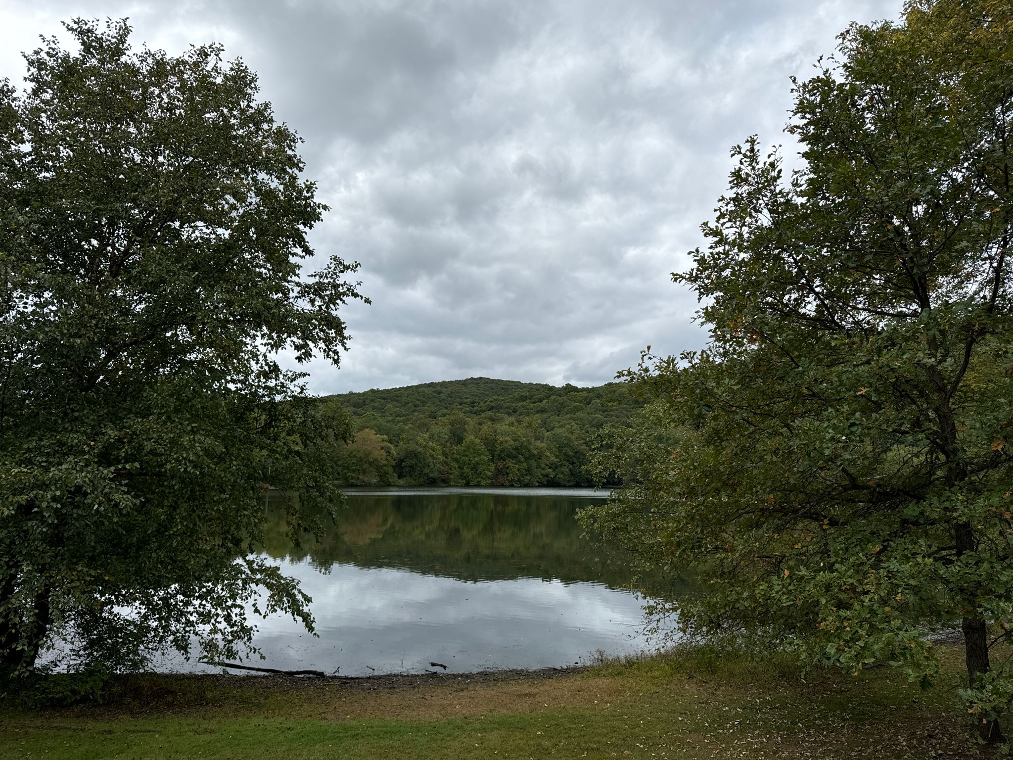 Calm lake reflecting cloudy sky, framed by trees and forested hills. - Lake Henry viewpoint – Ramapo River loop from Ramapo College of New Jersey
