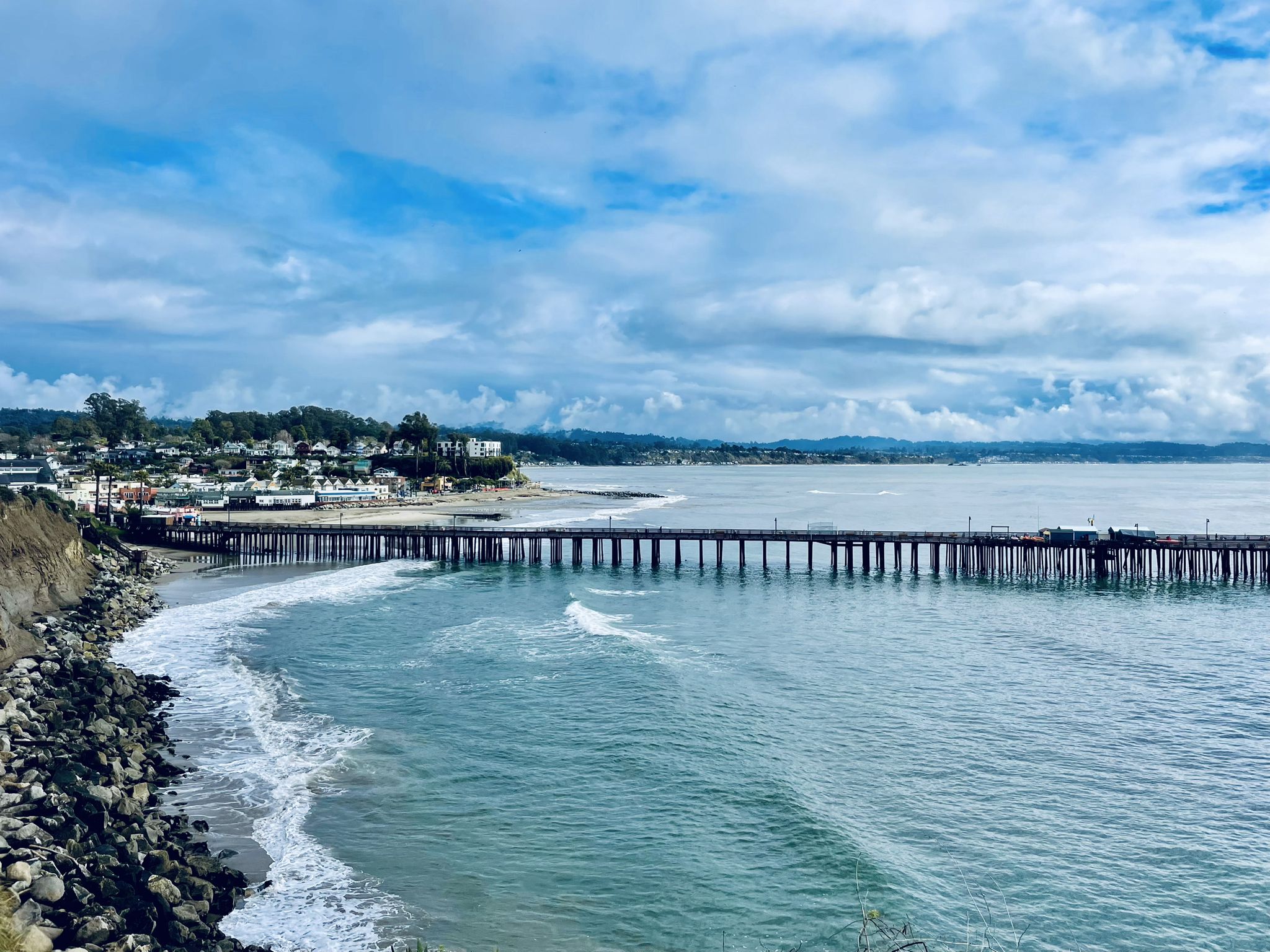 A long pier extends into the ocean with waves and a distant town. - Soquel-Aptos Creek Loop
