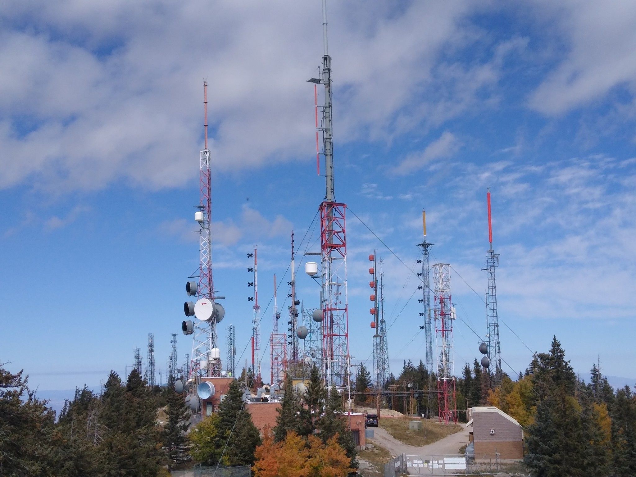 Numerous communication towers on a forested hilltop under a partly cloudy sky. - Sandia Crest Overlook – Sunset View from Sandia Crest loop from Cañoncito