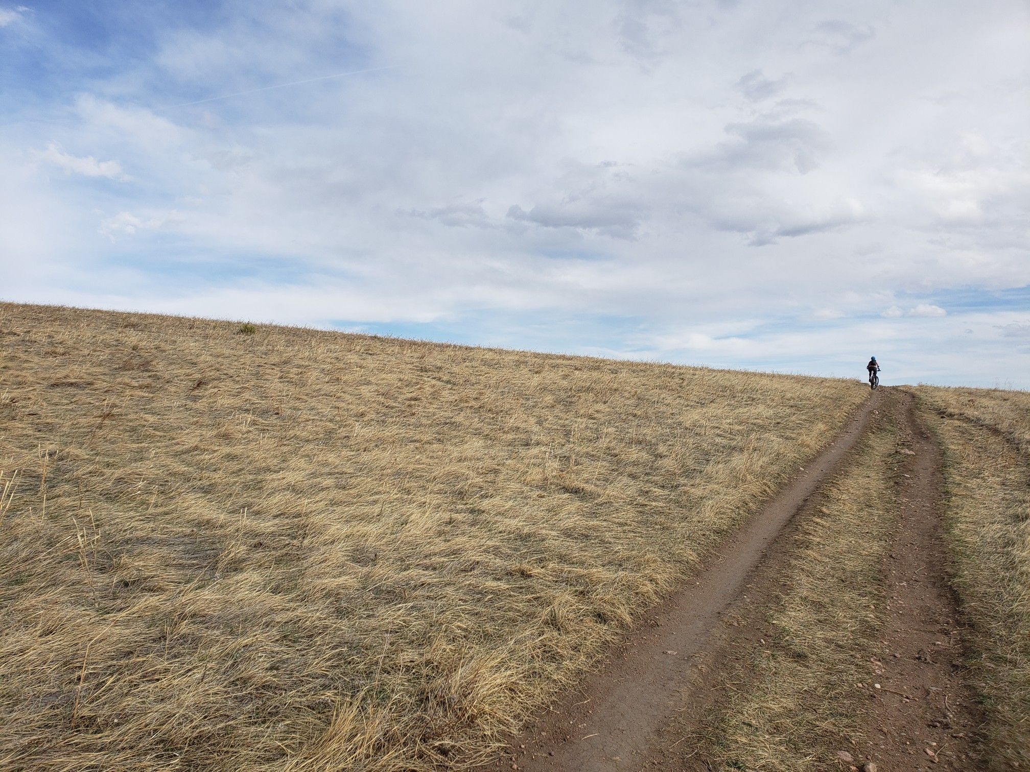 A cyclist rides up a dirt path on a dry grassy hill. - Green Mountain and Rooney Valley Loop