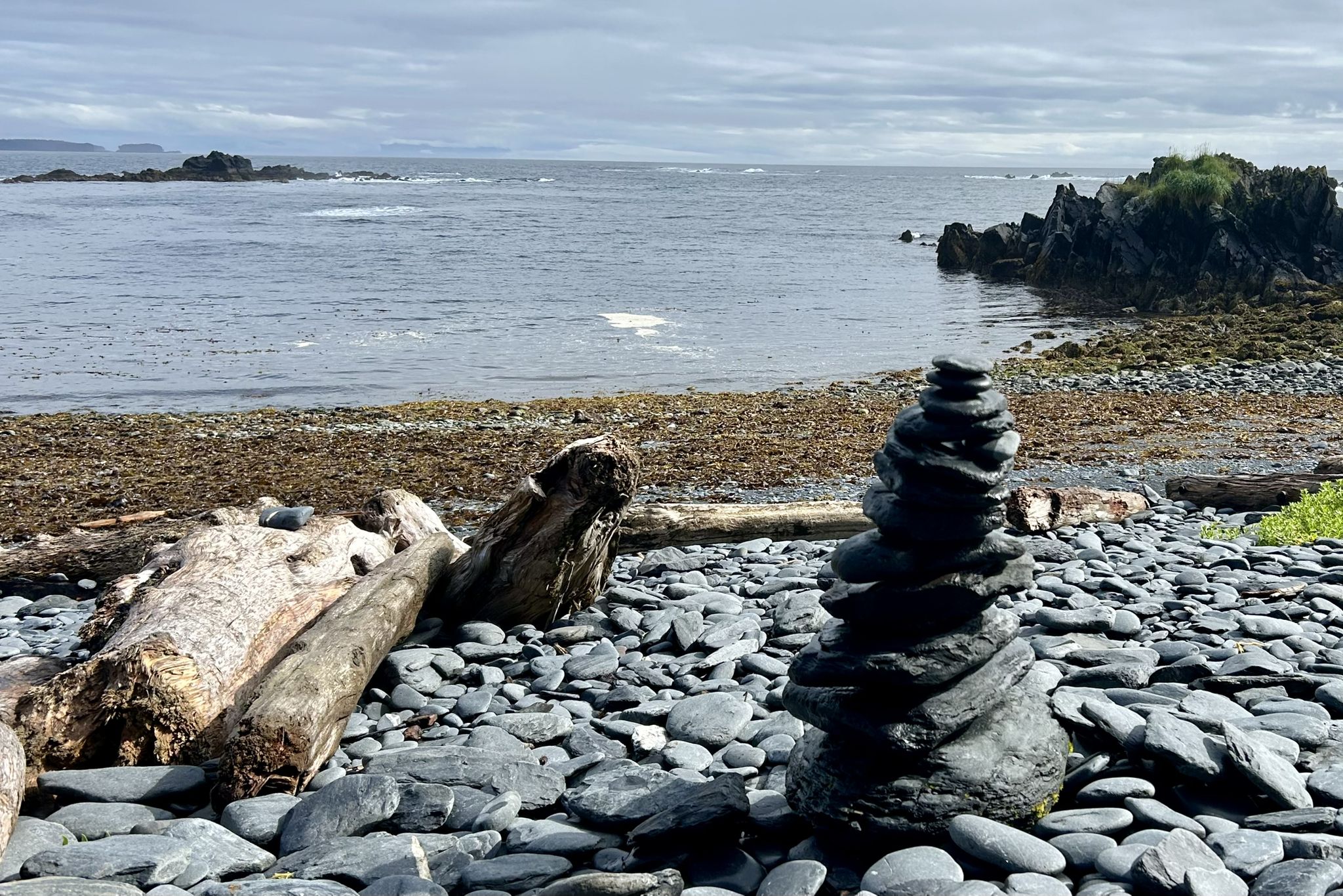 Stone cairn on a rocky beach with driftwood and ocean in background. - Fort Abercrombie Cliffs Loop