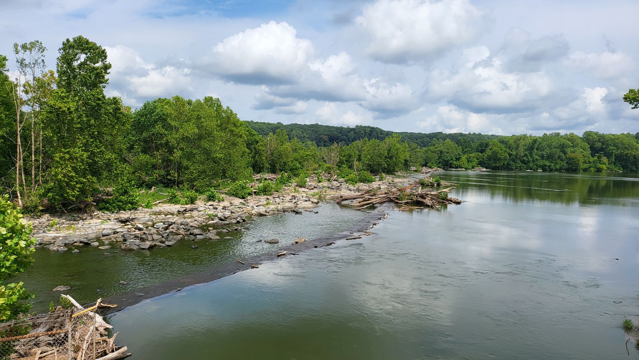 Wide river with rocky banks, lush green trees, and a partly cloudy sky. - Glen Echo Park – Angler's Inn parking lot loop from Bethesda