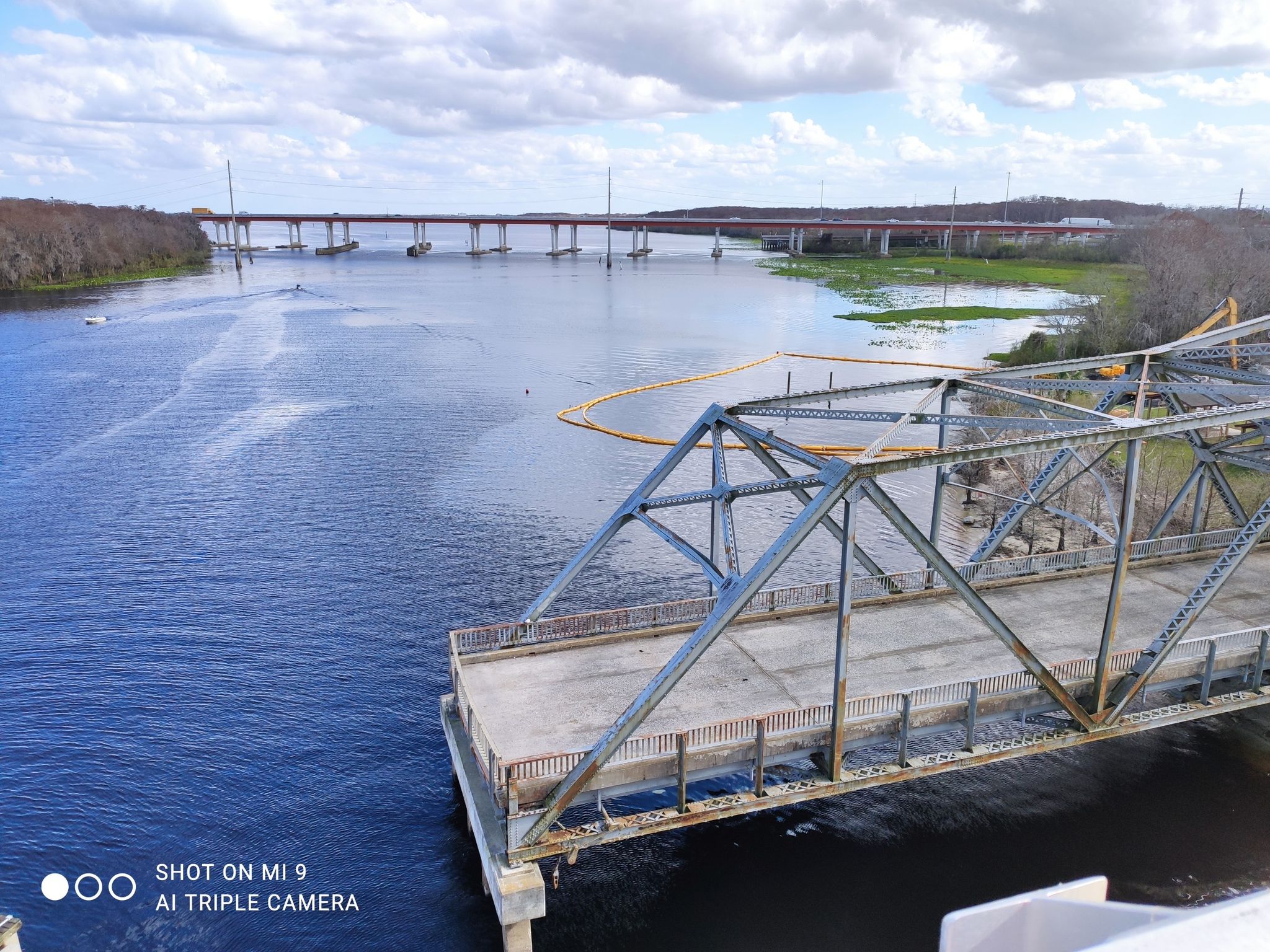 Metal truss bridge over a river with a distant bridge under cloudy sky. - Paint the Trail Artwork [Just past mile marker 7.25 EB] – Seminole Bridge loop from Altamonte Springs