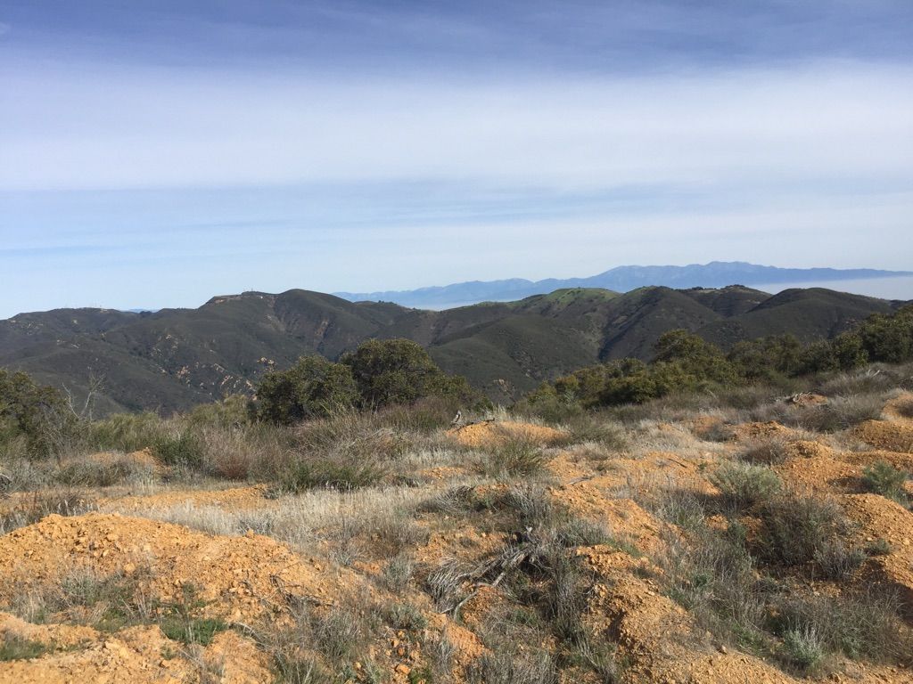 Dry, rocky foreground with distant green mountains under a hazy blue sky. - Silverado Motorway Trail