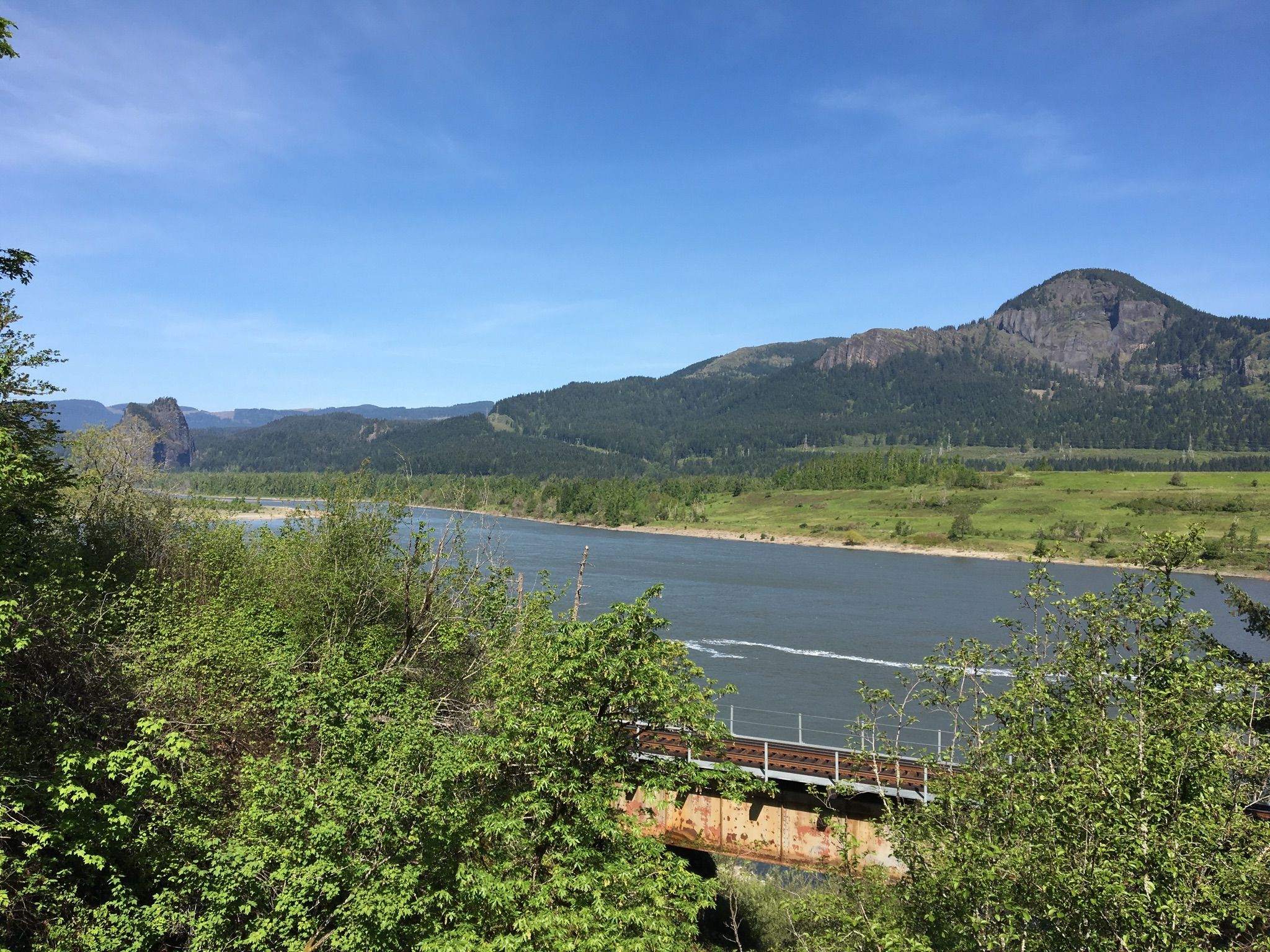 Wide river flows past forested mountains under a bright blue sky. - Historic Columbia River Highway State Trail