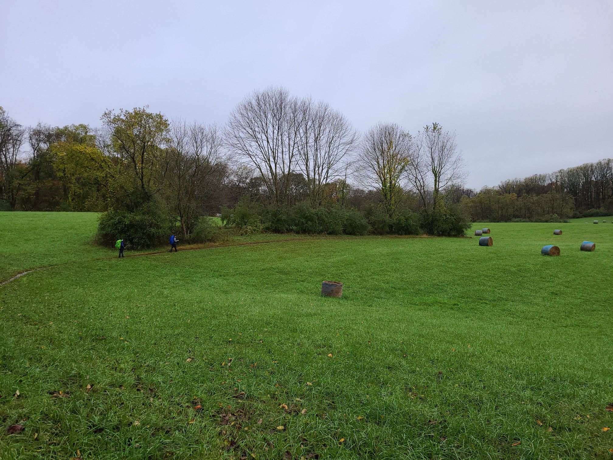 Overcast day in a green field with hay bales and two distant figures. - Ivy Branch, Farm Road, Deer Creek, and Susquehanna Ridge Trail