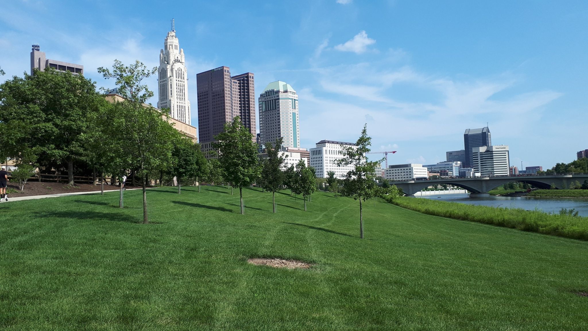 A green park with trees leads to a city skyline and river. - Scioto Trail – Historic Columbus Union Station Arch loop from Nationwide Arena