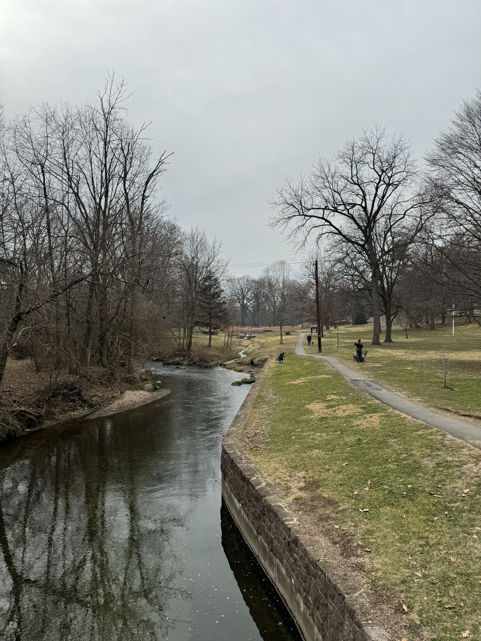 A river flows beside a path with bare trees under an overcast sky. - Wyomissing Creek and Schuylkill River Trail Loop