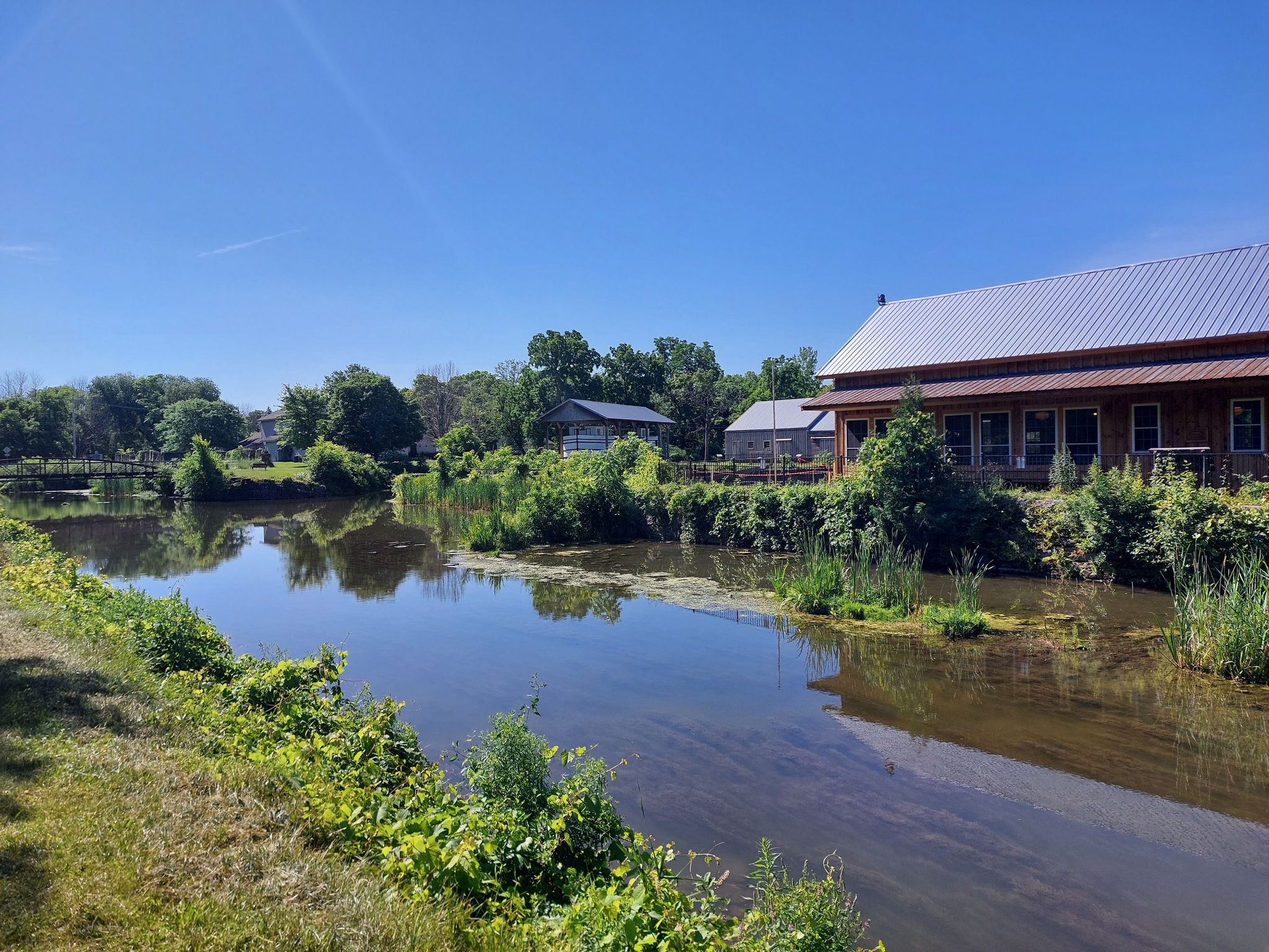 A calm waterway with reflections, surrounded by green trees and buildings on a sunny day. - Old Erie Canal Historical Park – Canal Overpass loop from Green Lakes State Park