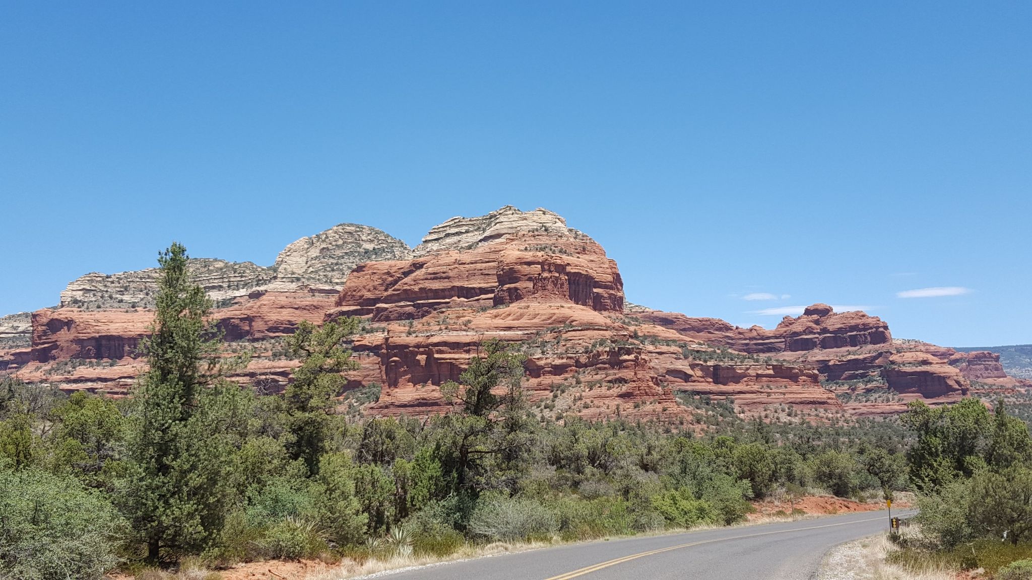 Towering red rock mountains above green trees and a road on a sunny day. - Fay Canyon Trailhead – Lover's Knoll loop from Soldiers Pass Rd