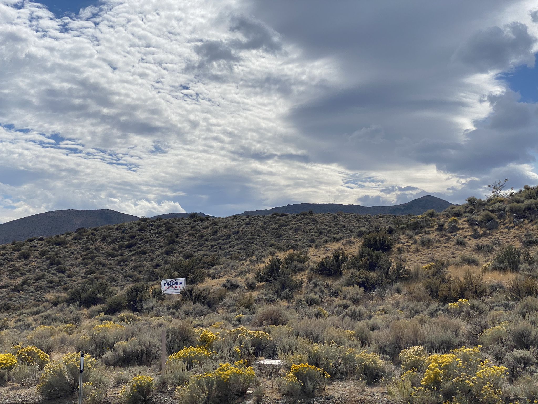 Arid hills under a cloudy sky, with sparse brush and a distant sign. - Galena Creek Visitor Center loop from Galena High School