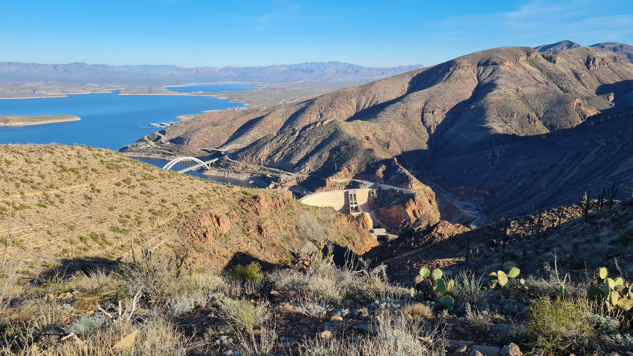Panoramic view of a blue lake, dam, and arid mountains under clear sky. - Vineyard Mountain – View of Bridge loop from Roosevelt Power Station