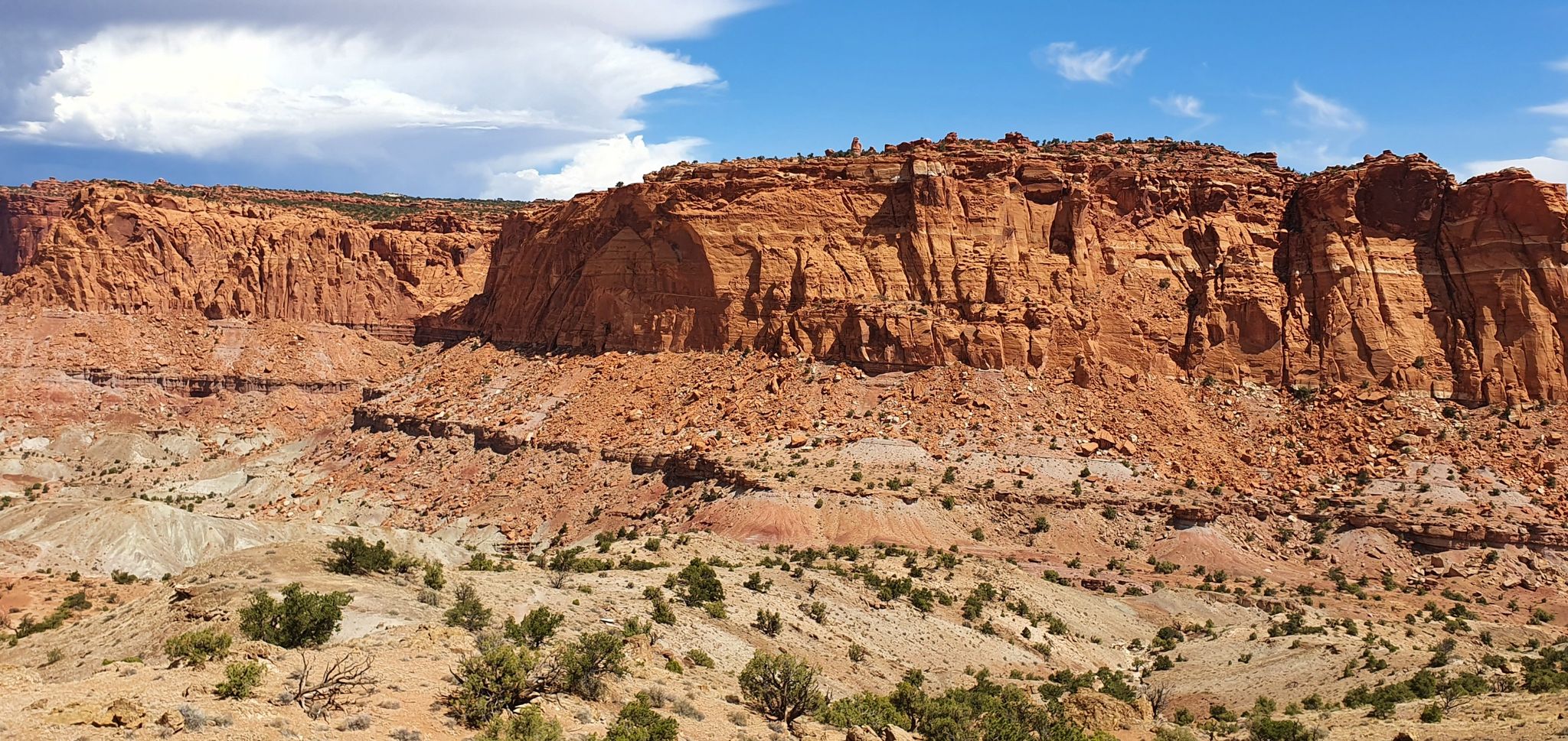 Expansive desert landscape with massive red rock cliffs under a partly cloudy sky. - Chimney Rock Loop Trail