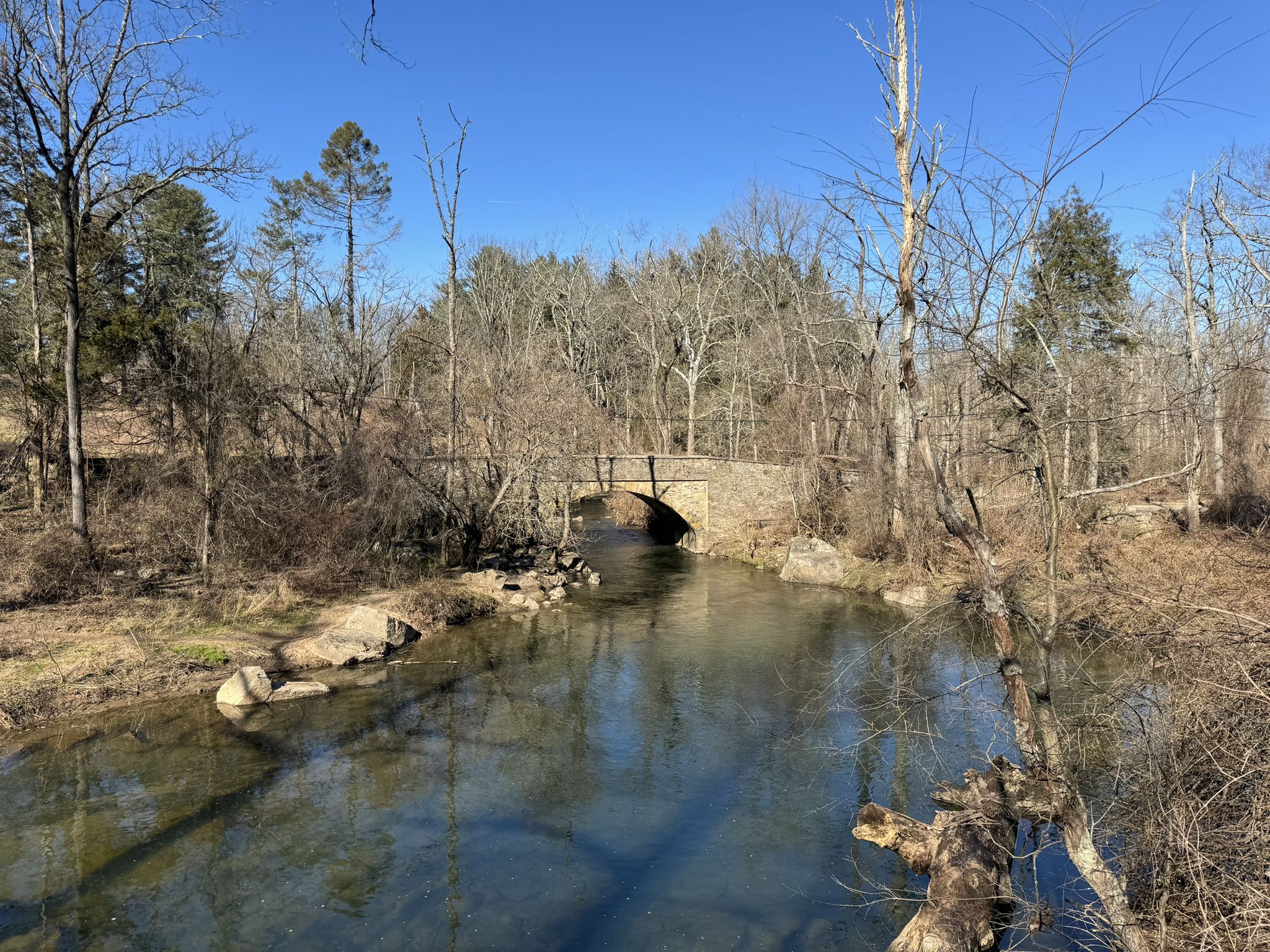 Stone arch bridge over a clear stream, surrounded by bare winter trees. - Newtown Rail Trail – Knight’s Bridge loop from Upper Southampton Township