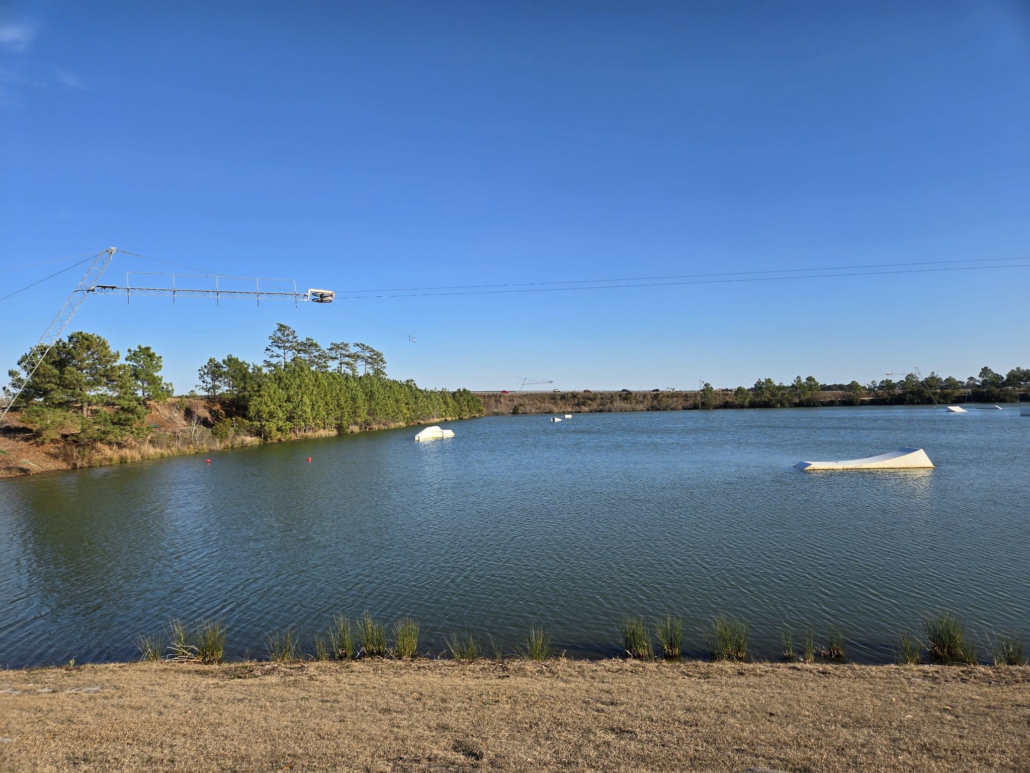 A lake with wakeboarding cables and obstacles under a clear blue sky. - NMB Nature Trail and Cypress Lake loop