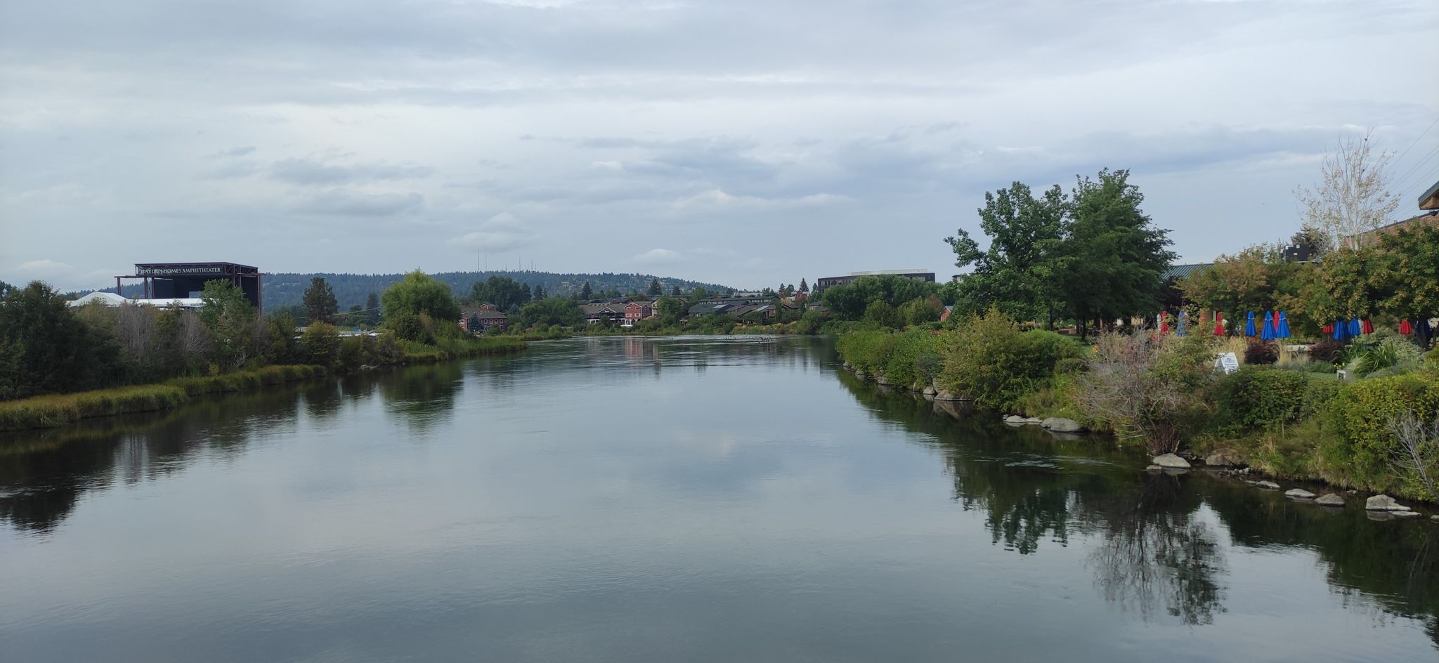 Calm river reflecting an overcast sky, with distant buildings and trees. - Drake Park – Drake Park loop from Deschutes Brewery