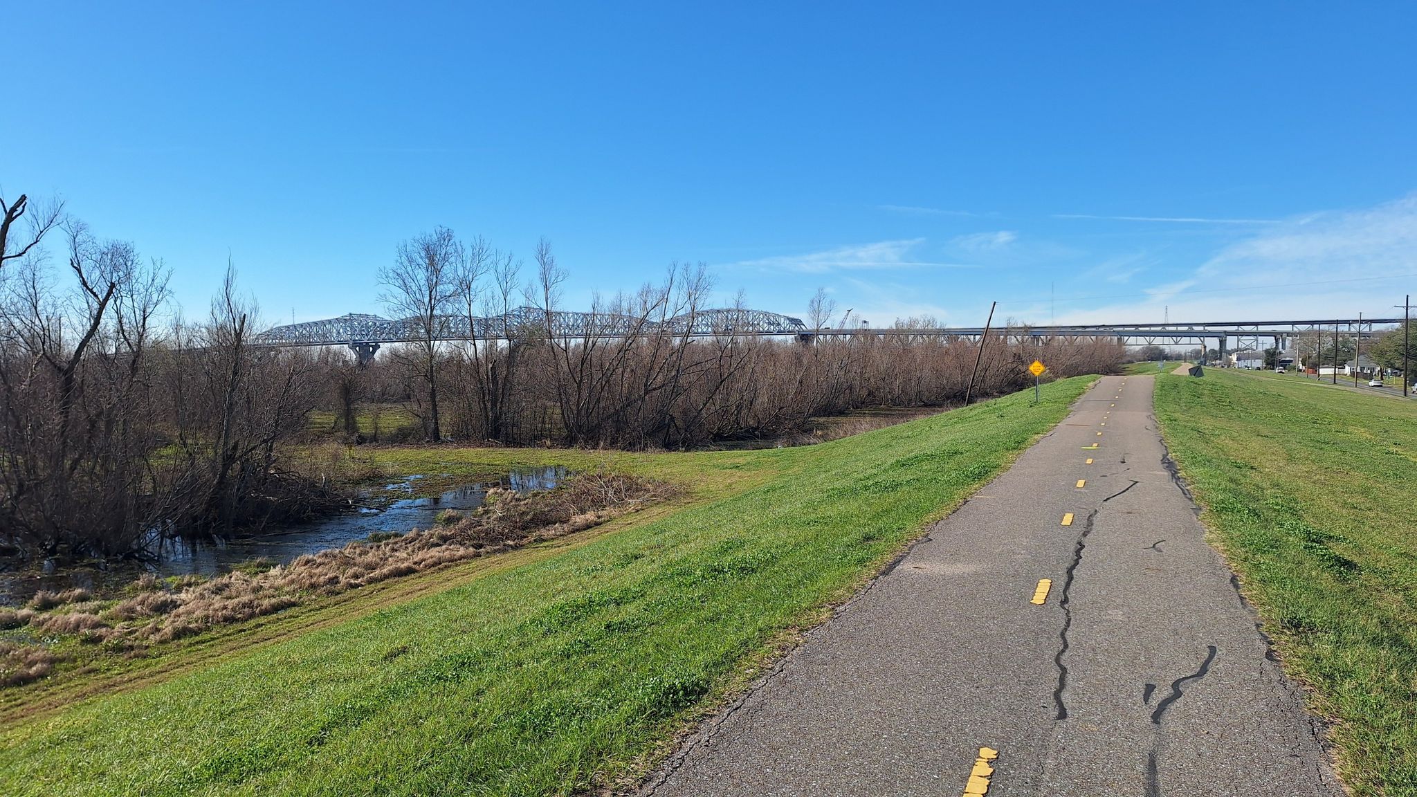 Paved path next to a river with bare trees and a distant bridge. - Mississippi River and Lake Pontchartrain Loop