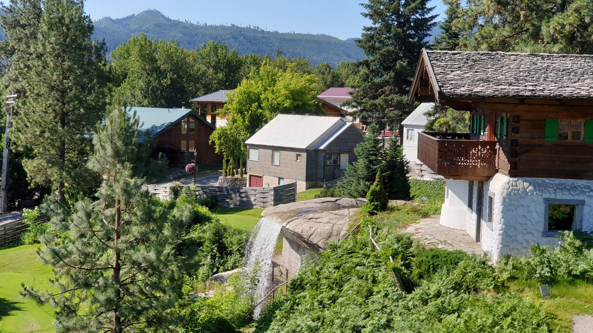 Rustic houses nestled on a sunny, green hillside with a small waterfall. - Wenatchee River loop