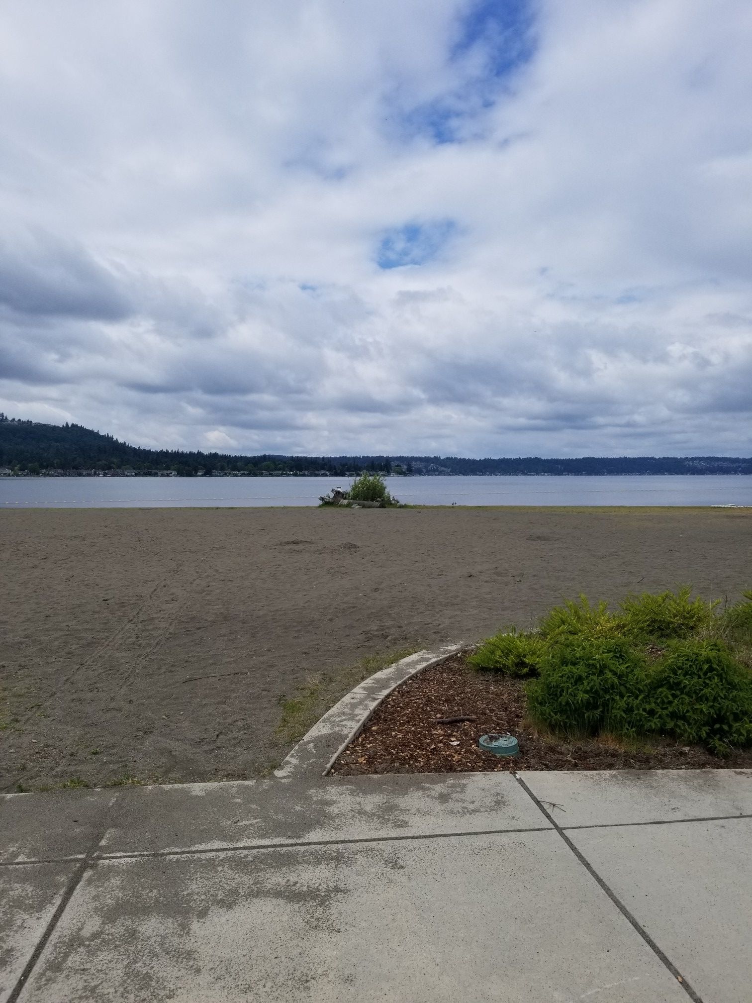 A wide, empty sandy beach meets calm water under a cloudy sky. - Tibbets and Sunset Beaches loop