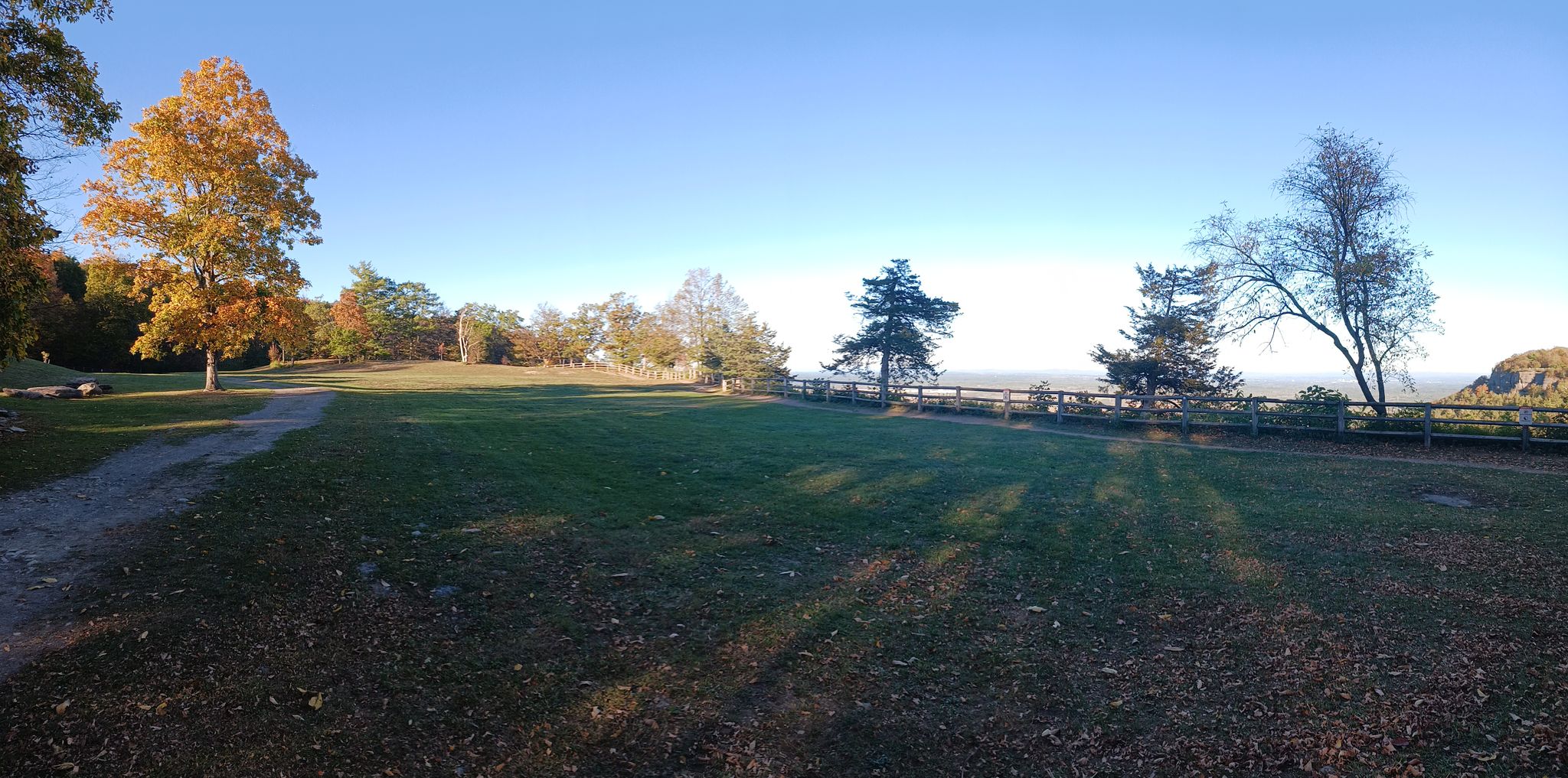 Sunny, open grassy field with scattered trees and a distant overlook railing. - Hiking trail along the cliffs – Waterfall at Thacher Park loop from Thacher State Park