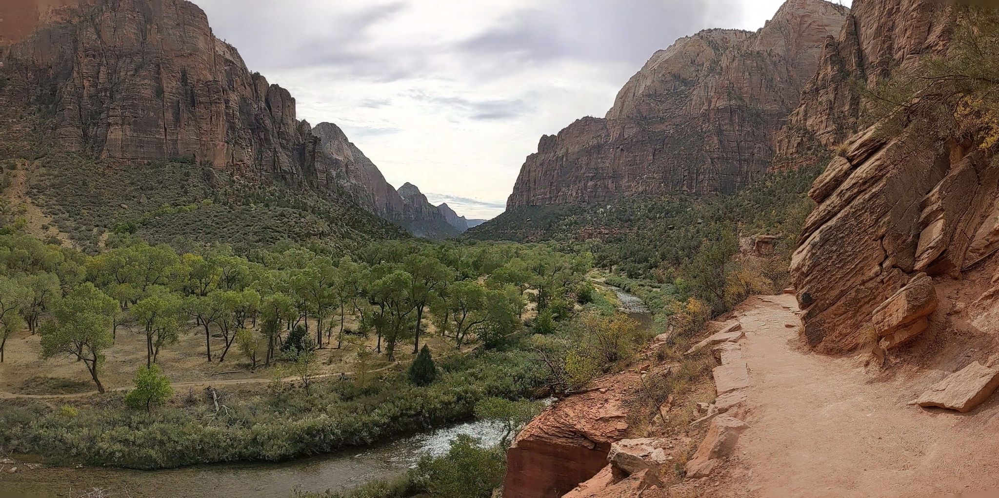 Panoramic view of a wide valley with a river, green trees, and red cliffs. - Sand Bench and Kayenta Trail