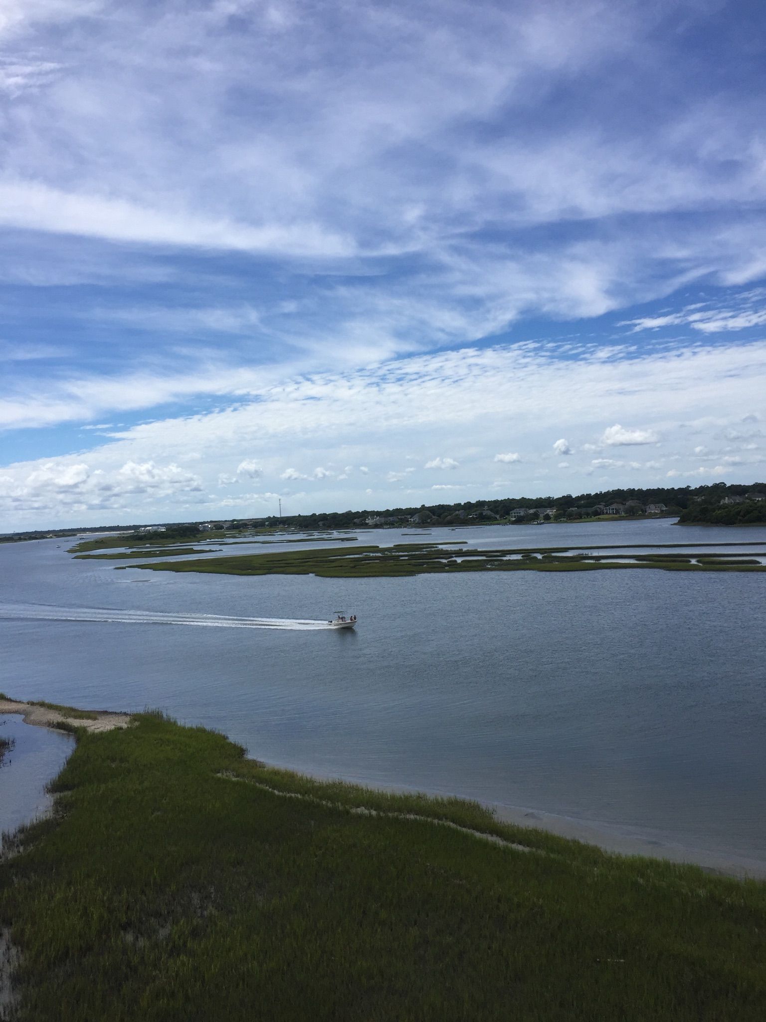 A boat speeds across wide water with marshy islands under a cloudy sky. - Fort Macon State Park – Fort Macon loop from Cape Carteret