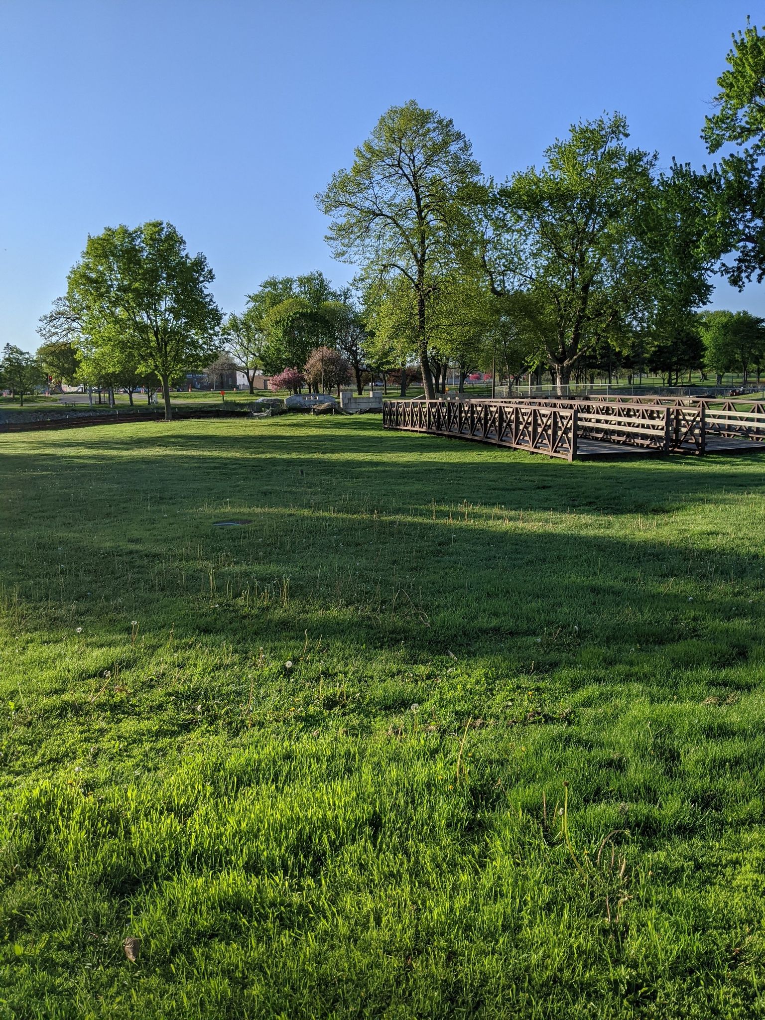 Sunny green field with a wooden bridge and trees under a clear sky. - Zumbro River Trail – Zumbro River Trail loop from Rochester