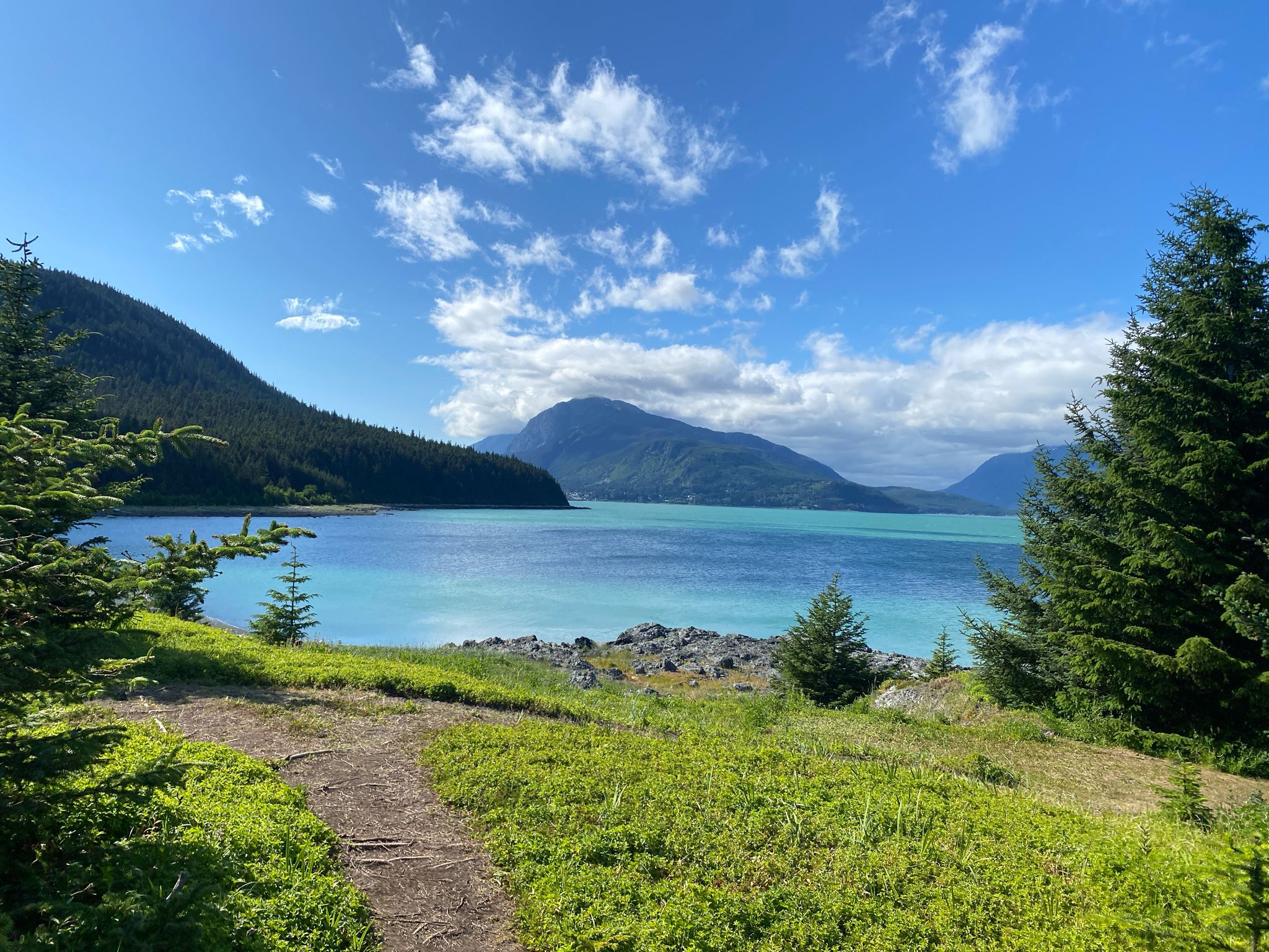 Sunny day, dirt path leading to turquoise water, mountains, and blue sky. - Mount Riley and Battery Point Trail