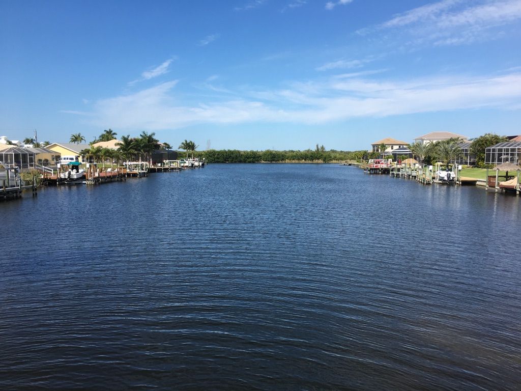 A wide, calm canal bordered by houses and docks under a clear blue sky. - Cape Coral loop