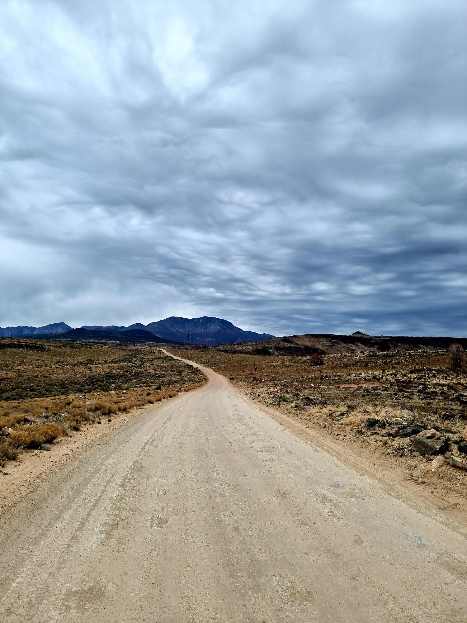 Long dirt road stretching towards distant mountains under a cloudy sky. - Broken Mesa - Ice House Loop