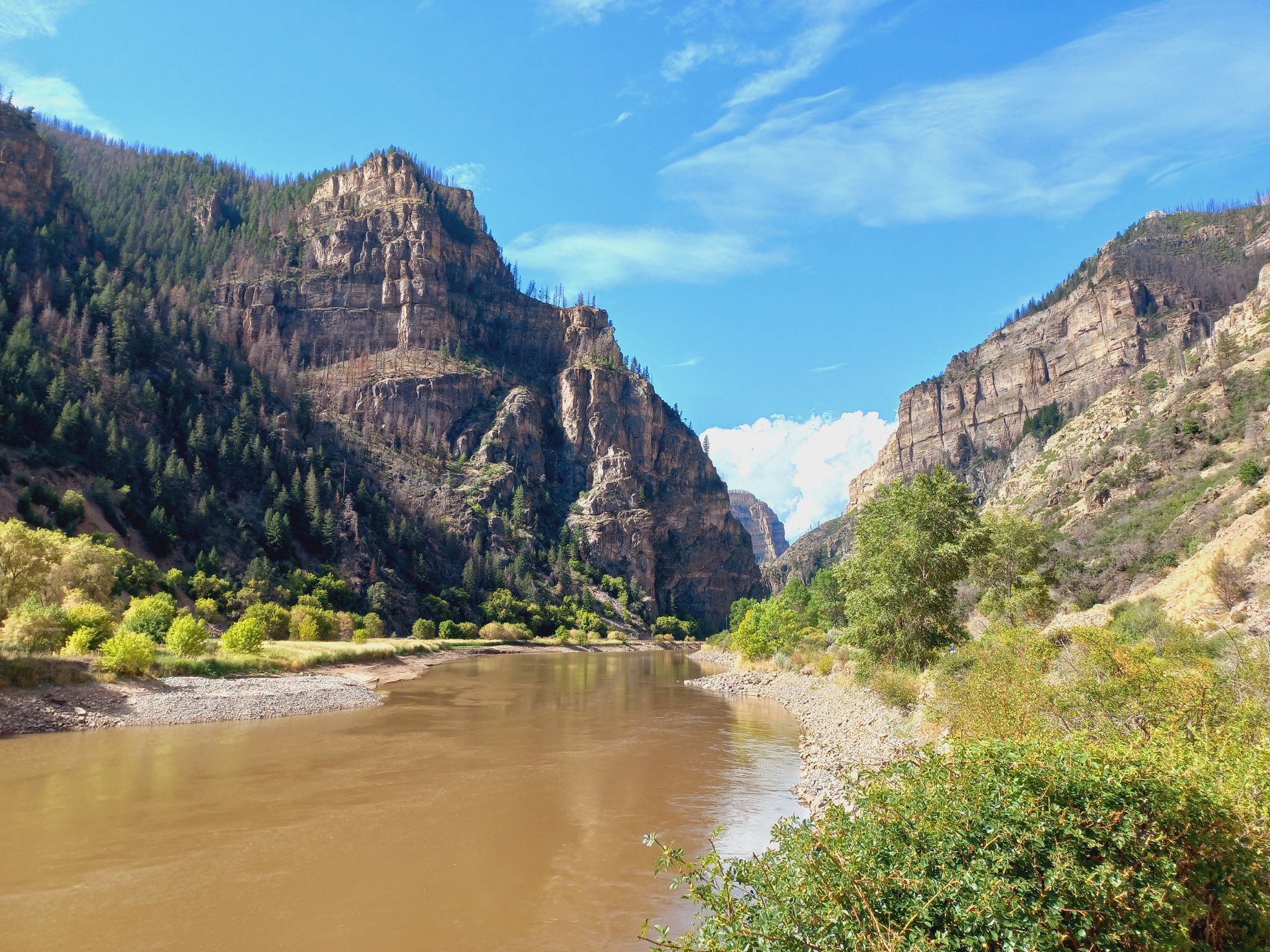 Wide river flowing between tall, forested canyon walls under a bright blue sky. - Hanging Lake Trail