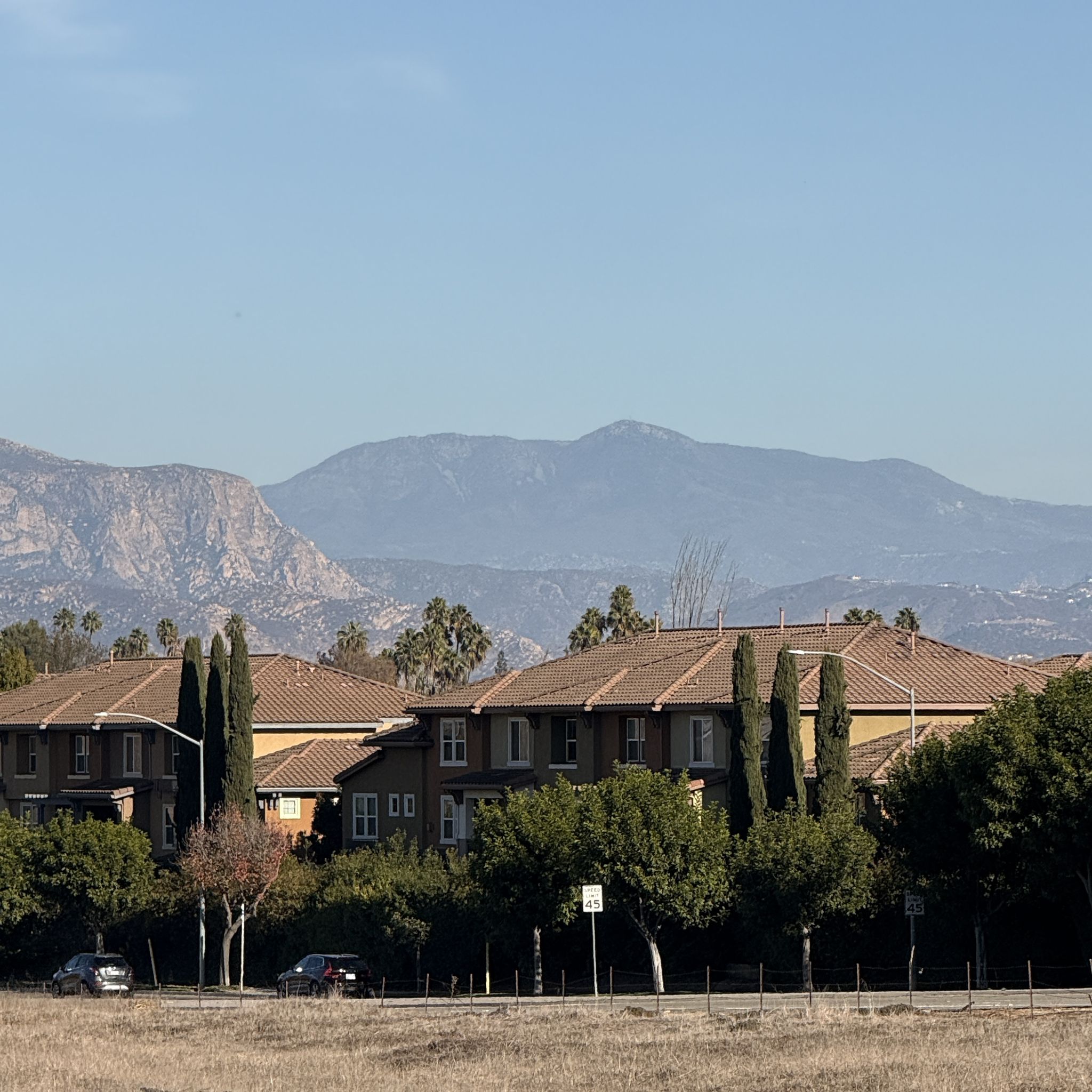 Residential buildings with tiled roofs and tall trees against hazy distant mountains. - SR 52 Bike Path – Mission Trails Regional Park loop from San Carlos