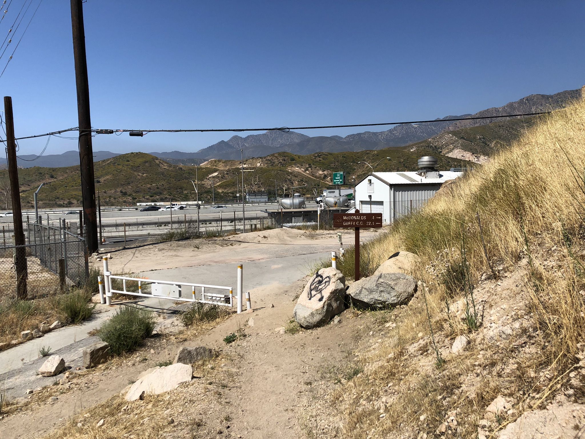 Dirt path leads to an industrial area with distant mountains on a clear day. - Pacific Crest Trail to Crowder Canyon
