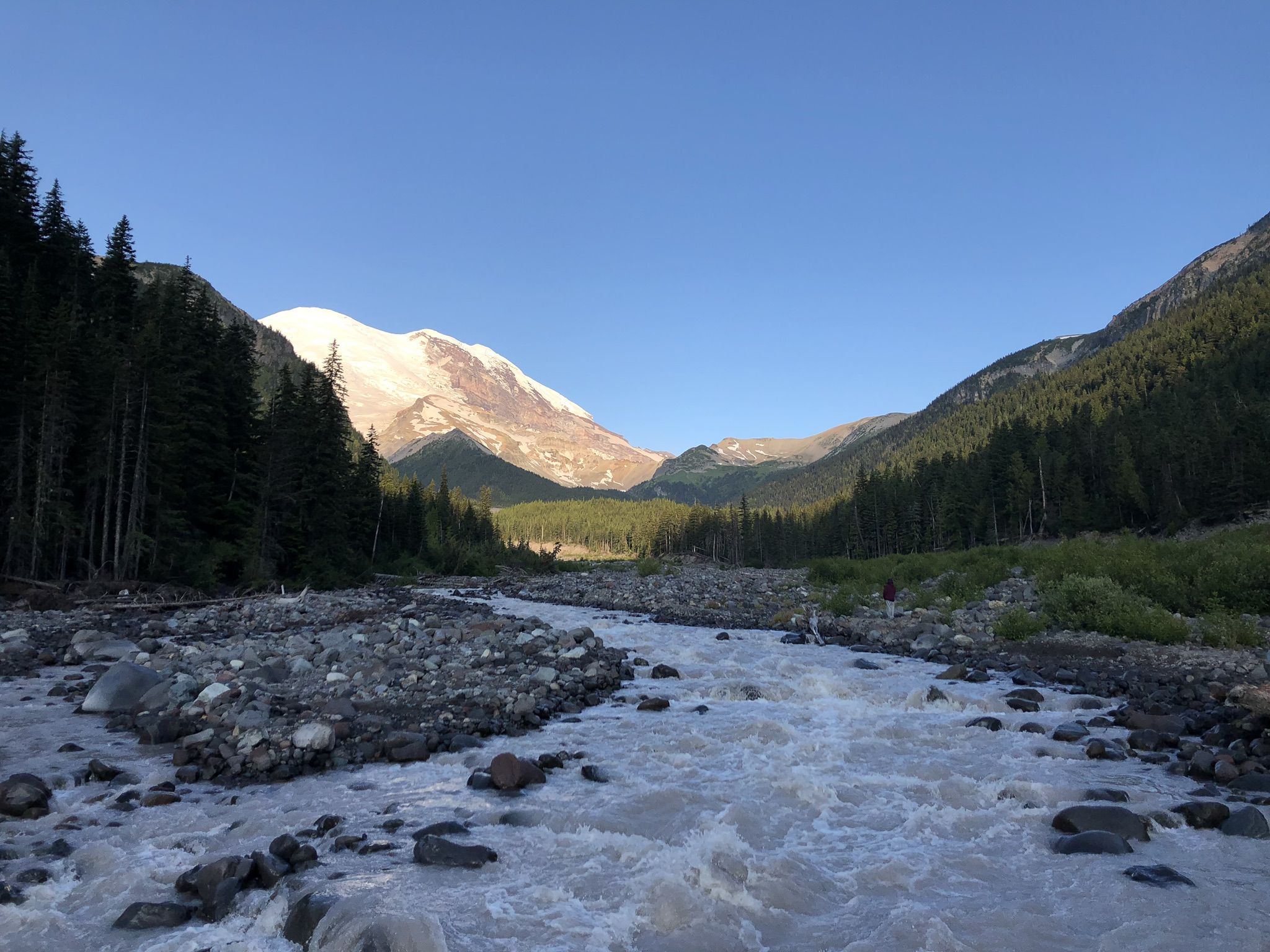 A wide, rocky river flows through a valley with forests and a snow-capped mountain. - Wonderland Trail: White River Campground to Box Canyon