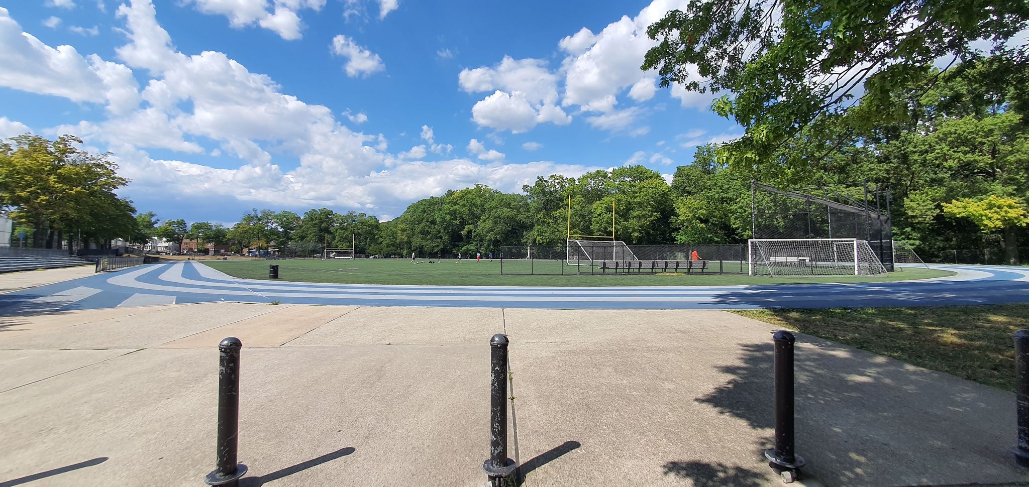 Sunny sports field with a blue track, green grass, and trees. - Brooklyn-Queens Greenway Loop