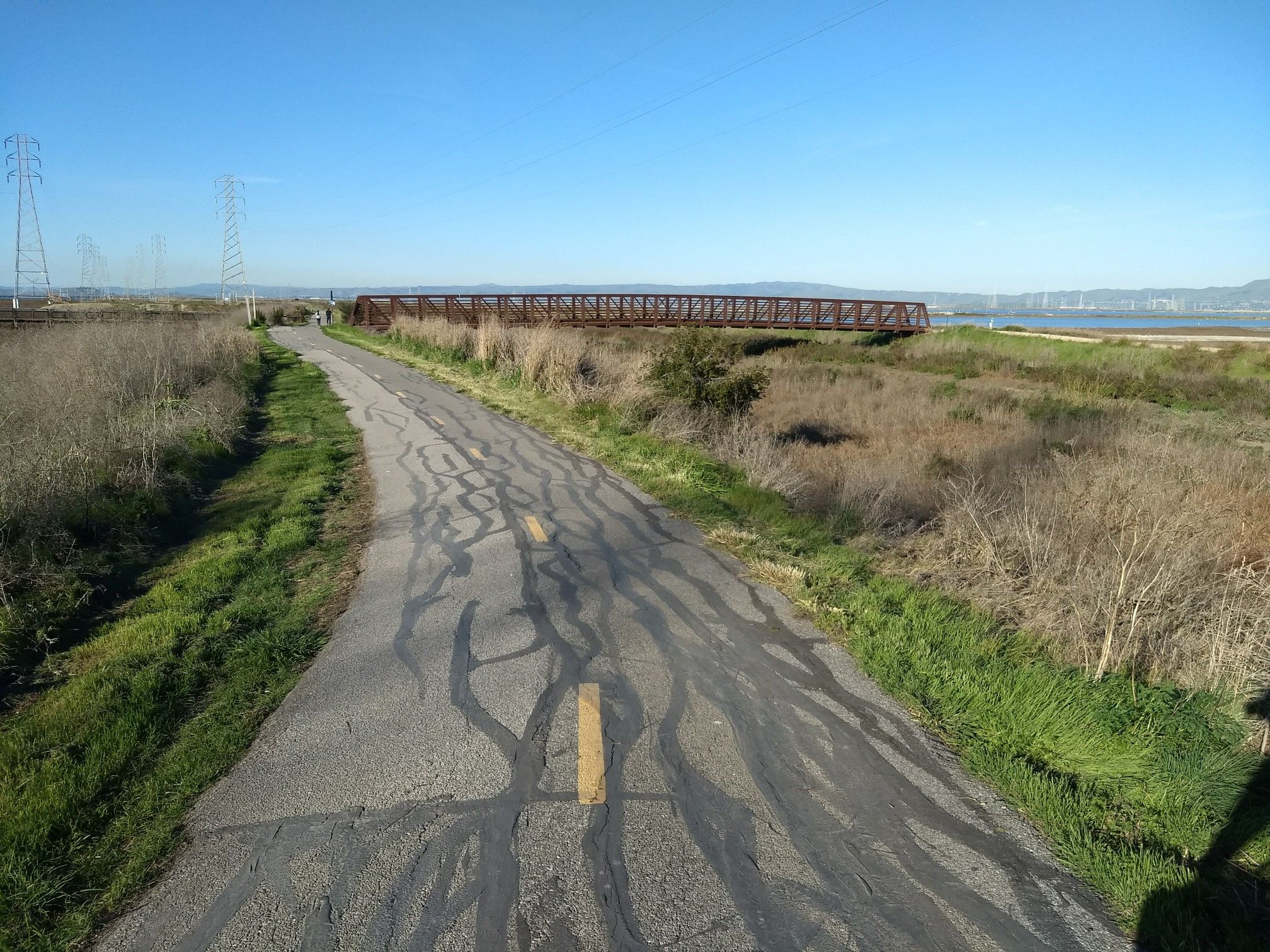 Paved path with tire marks, distant bridge, power lines, sunny day. - Stevens Creek Trail loop from Computer History Museum