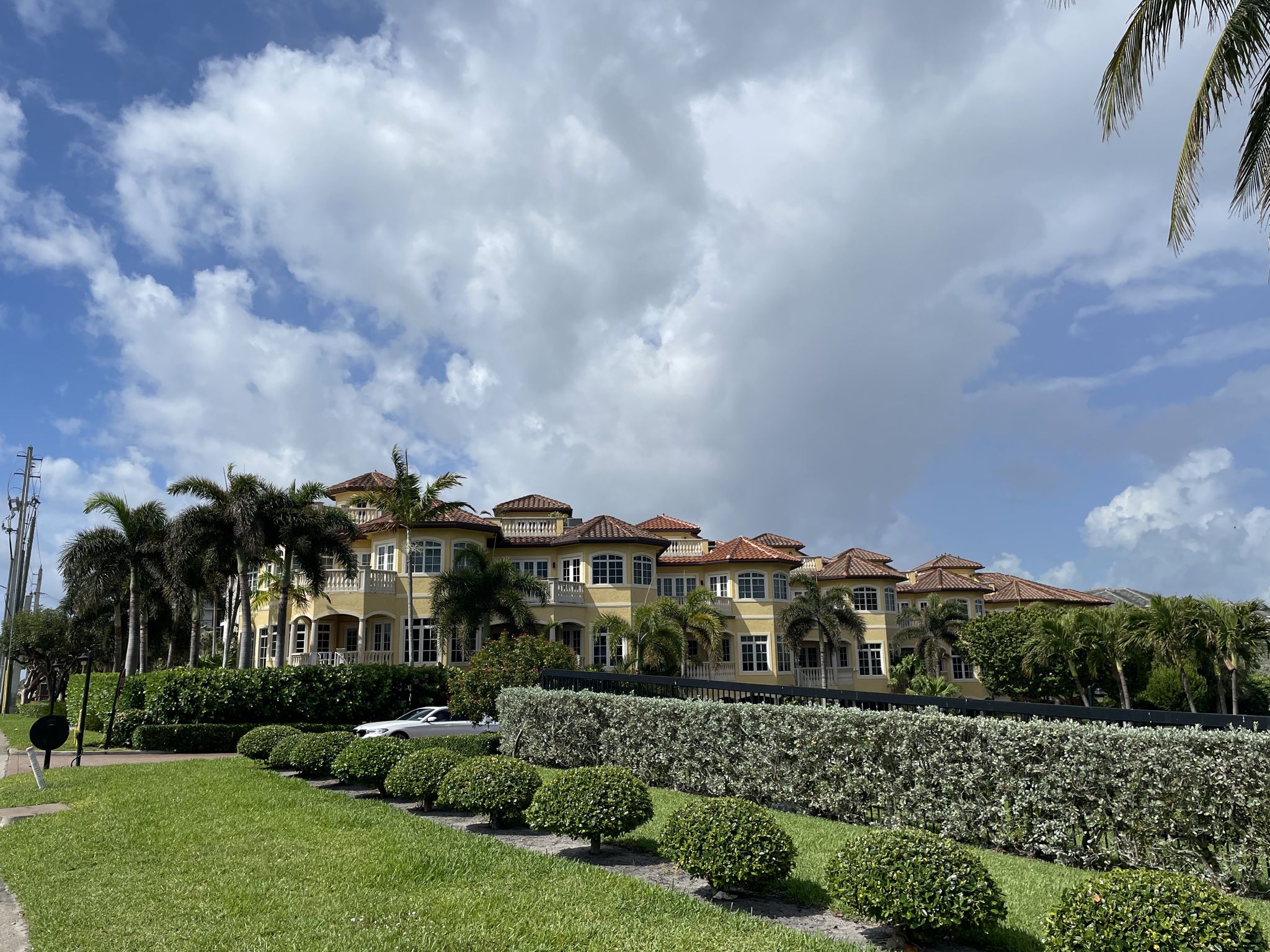 Large yellow building with red roofs, palm trees, and hedges under a cloudy sky. - East Coast Greenway and El Rio Trail Loop