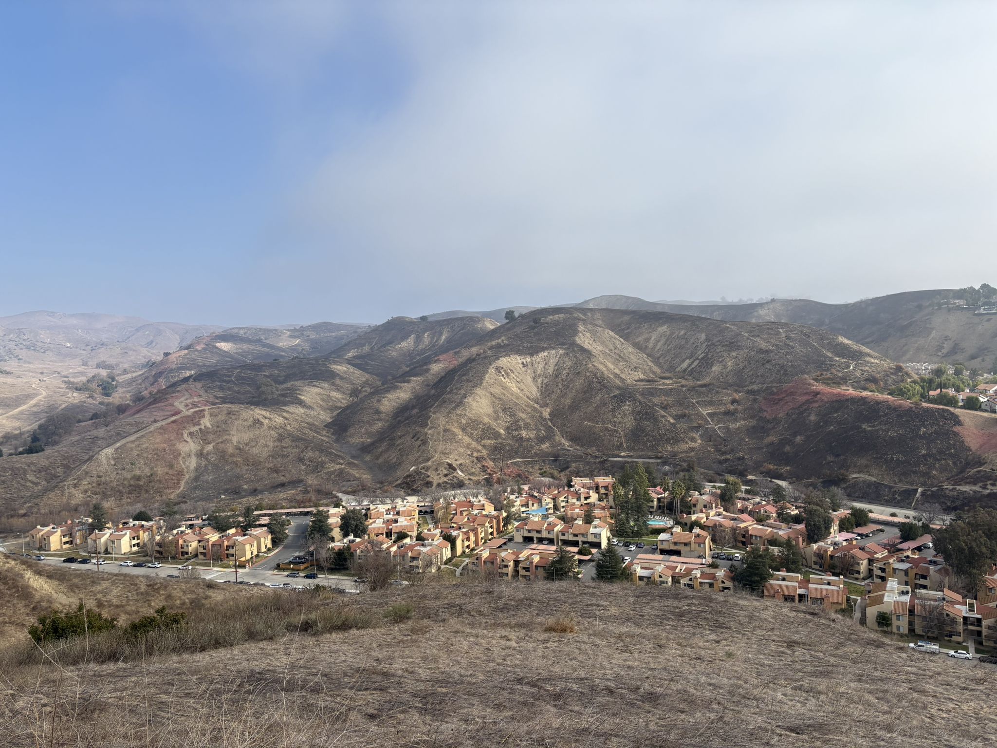 Residential buildings nestled in dry, rolling hills under a hazy blue sky. - Las Virgenes Creek – East Las Virgenes Canyon loop from Liberty Canyon Open Space